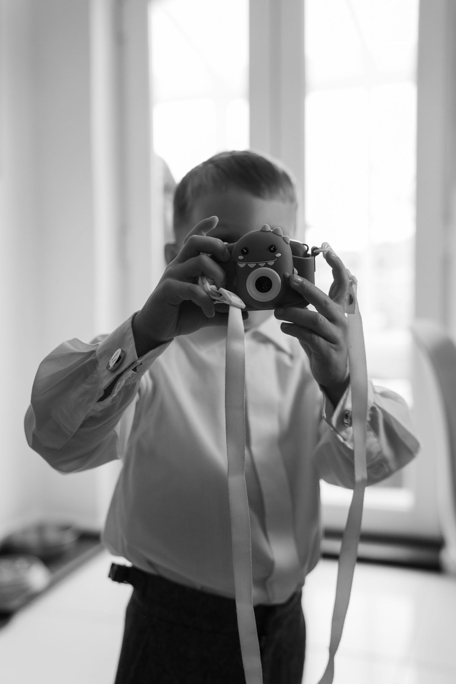 Black and white photo of someone holding a vintage camera in a bright room with windows.