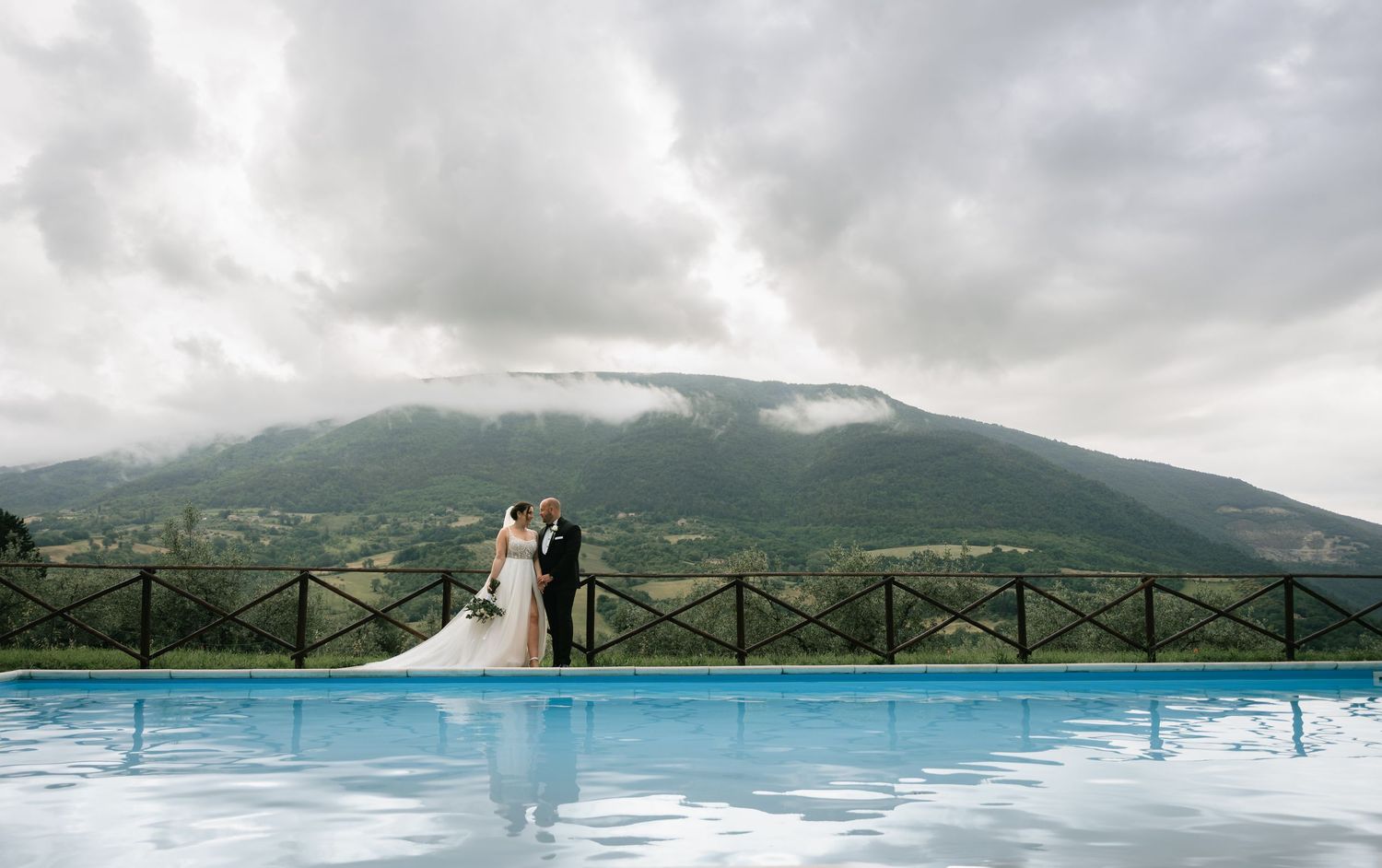 A panoramic view of a mountain landscape with a cloudy sky and lake reflecting the dramatic scenery.