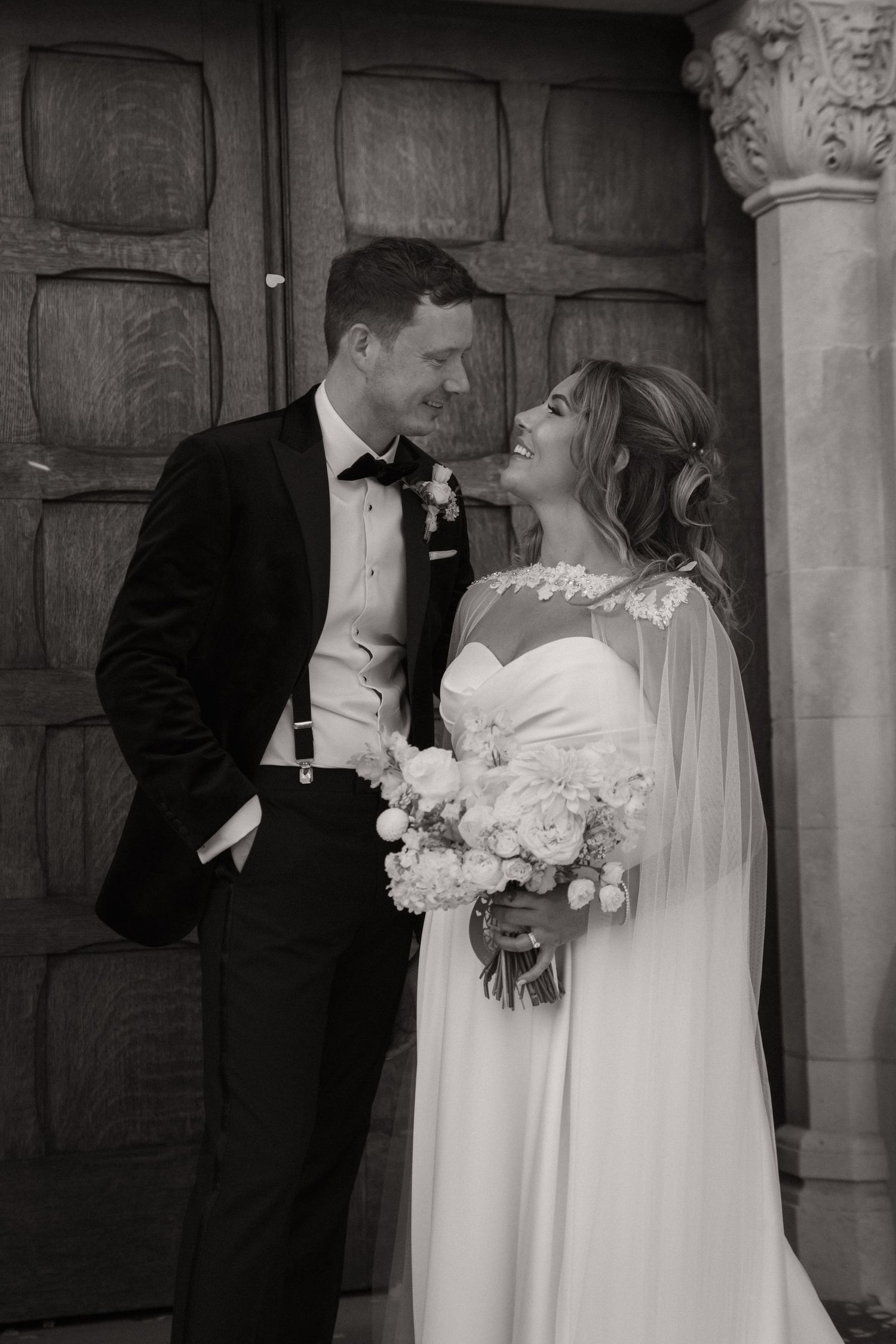 Black and white wedding photos show romantic moments between bride in white dress and groom in tuxedo against stone wall.