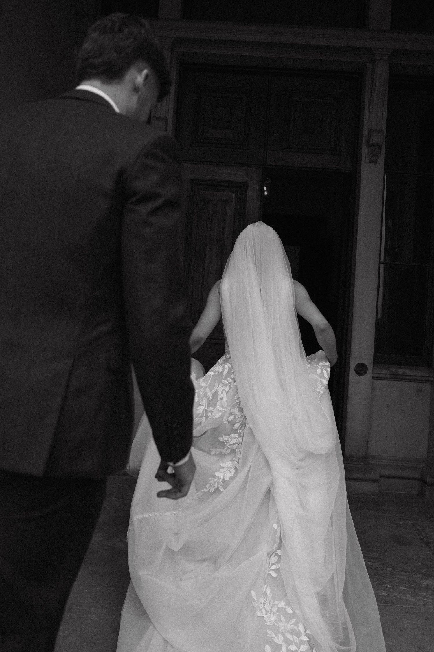 Elegant wedding dress and veil trailing behind as couple walks together.