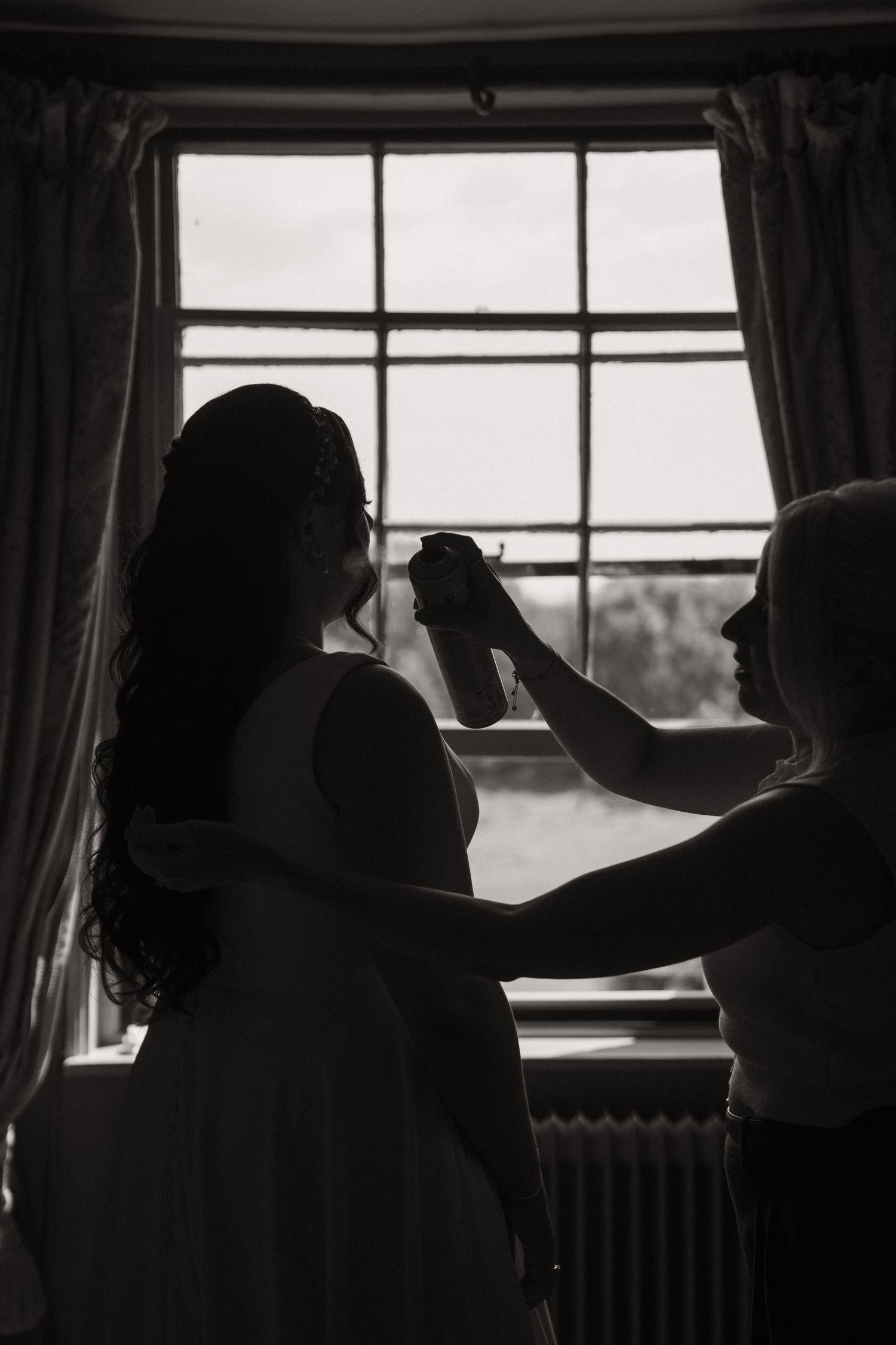 Silhouettes of people adjusting curtains by a window in a dimly lit room, creating a dramatic contrast.
