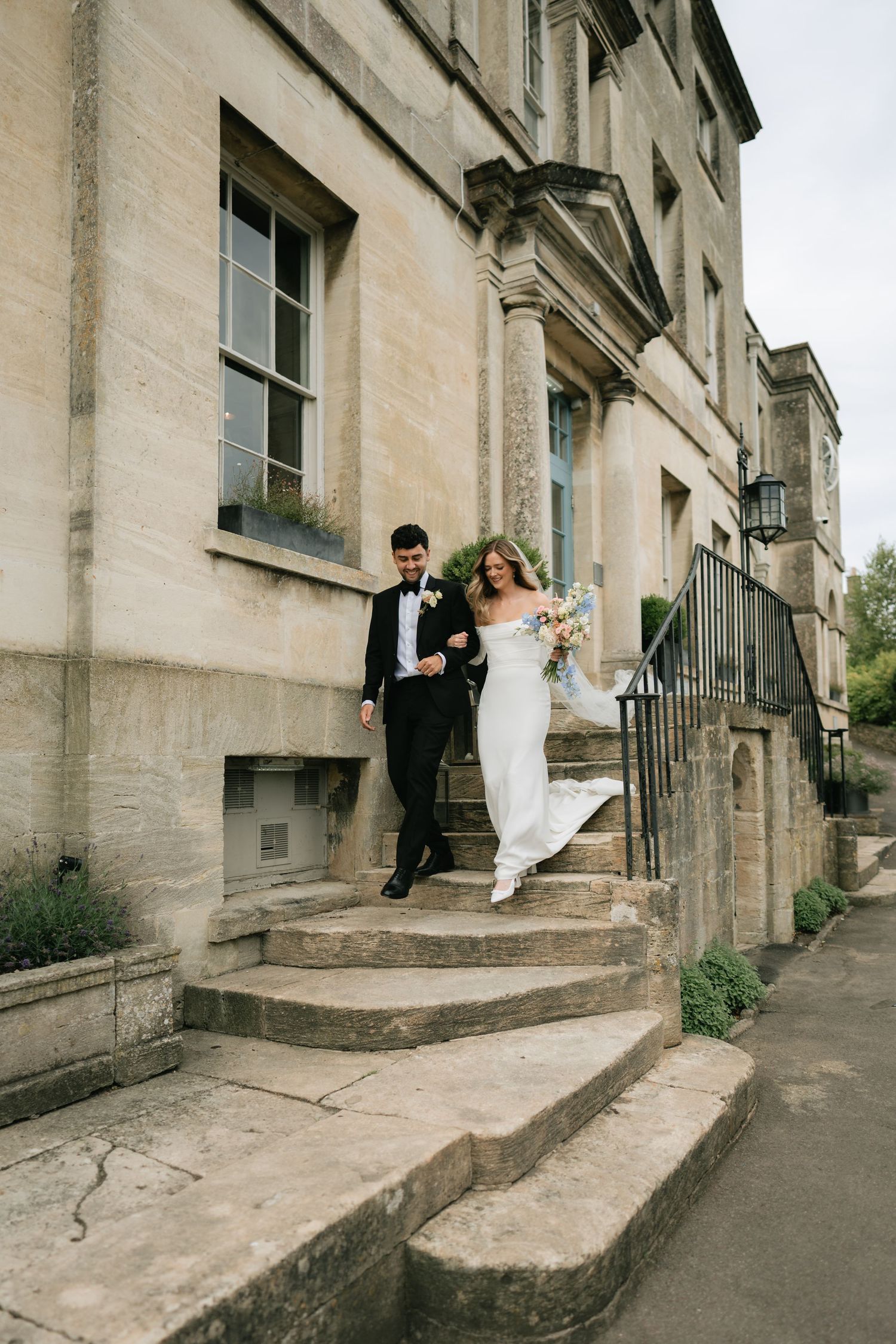 A series of five wedding photos showing a couple descending stone steps outside a historic building in playful poses.