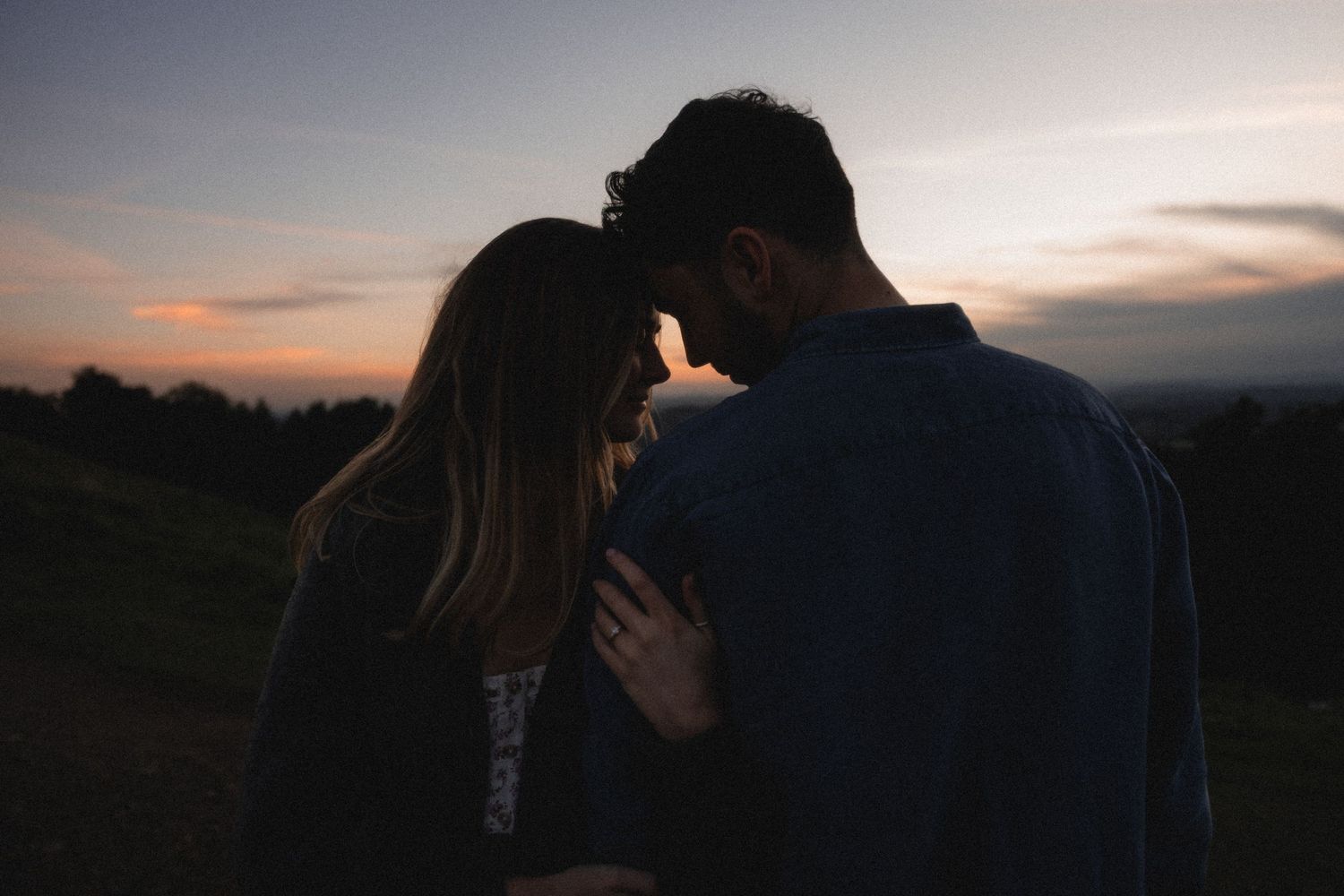 Silhouettes of a couple embracing against a dramatic sunset sky.
