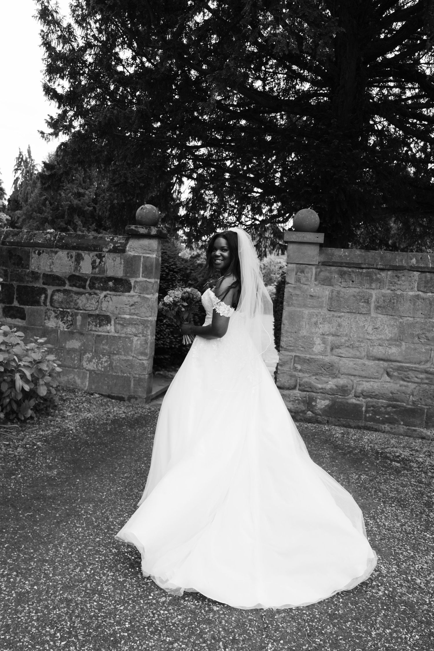 Wedding dress twirling against stone wall in black and white photography.