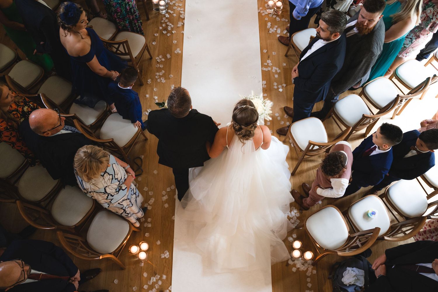 Wedding guests gather around a dance floor at a reception venue with elegant lighting and decor.