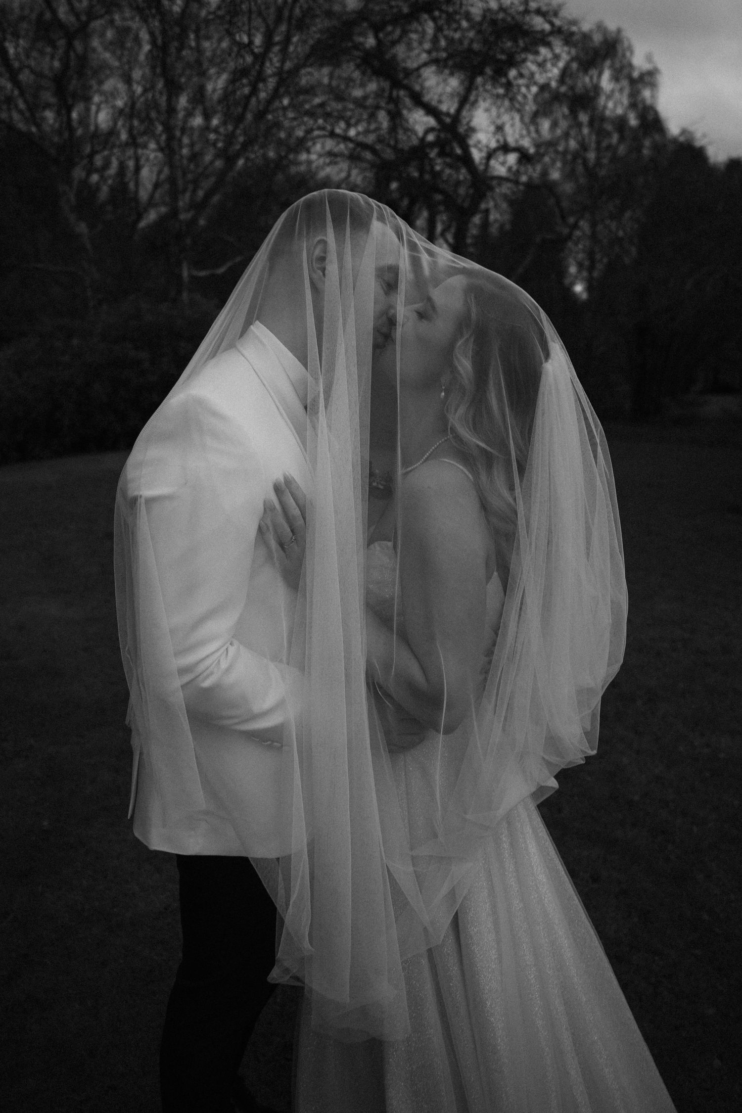 A romantic black and white photo series showing a couple embracing under a flowing white veil in a dreamy outdoor setting.
