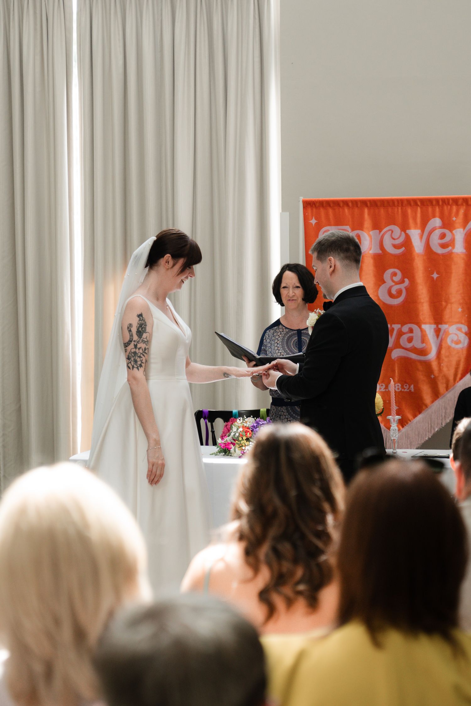 A crowd watches a presentation in a bright room with orange banners visible in the background.