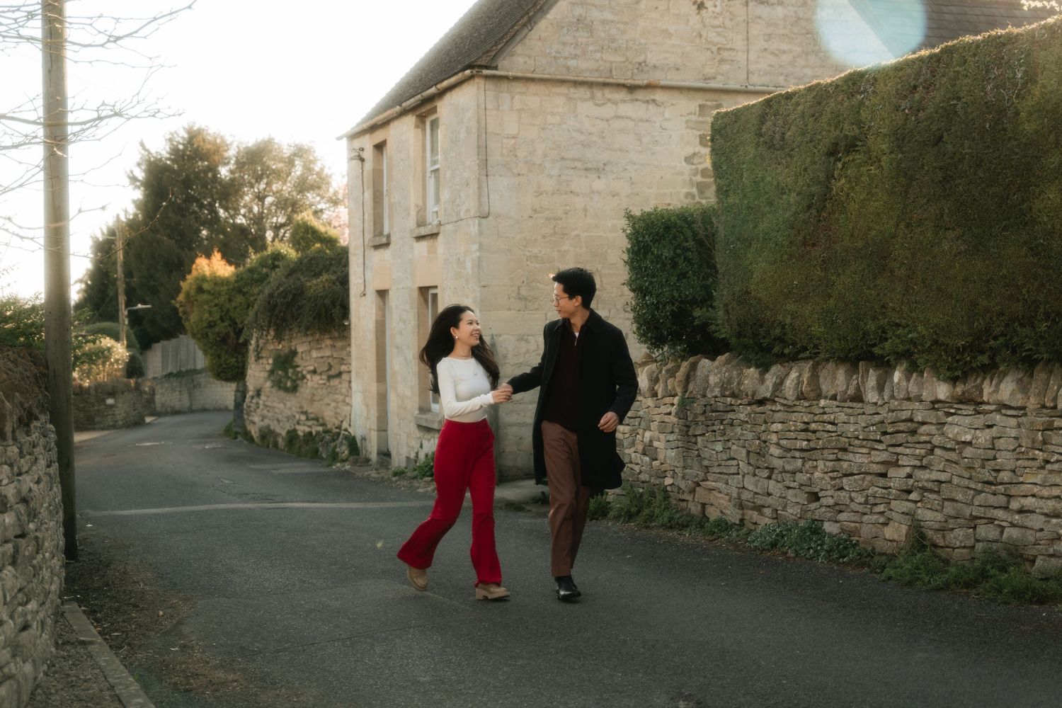 Couple walking together along stone wall lined street at sunset.