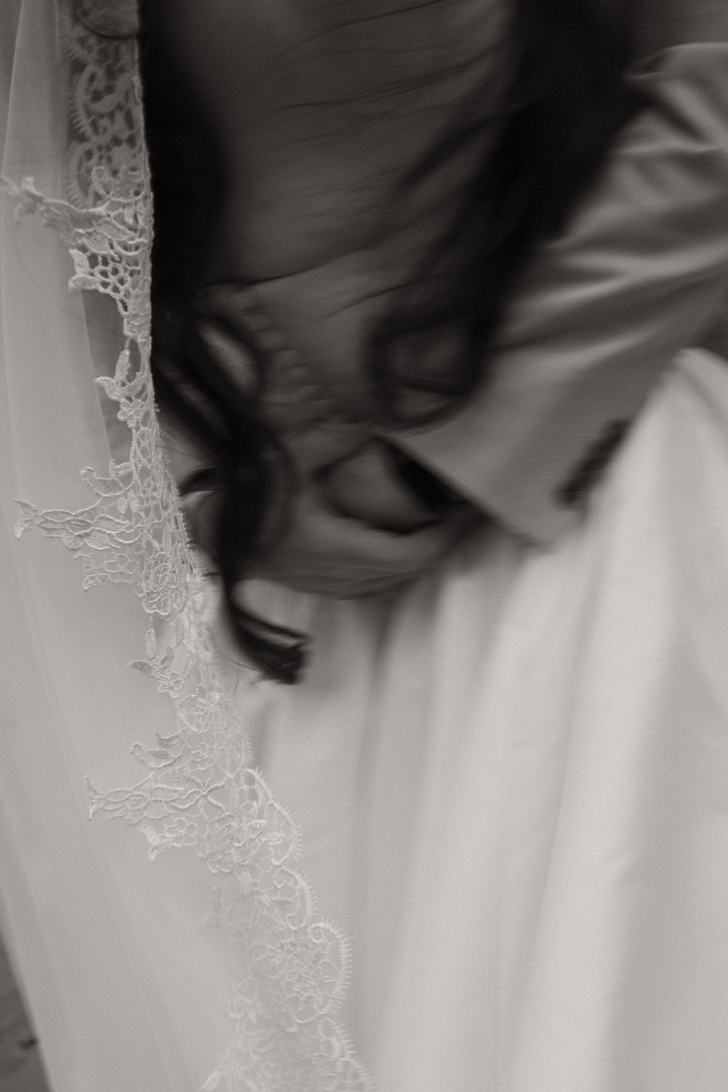 Black and white photo of a bride in lace veil and gown with flowing dark hair on her wedding day.