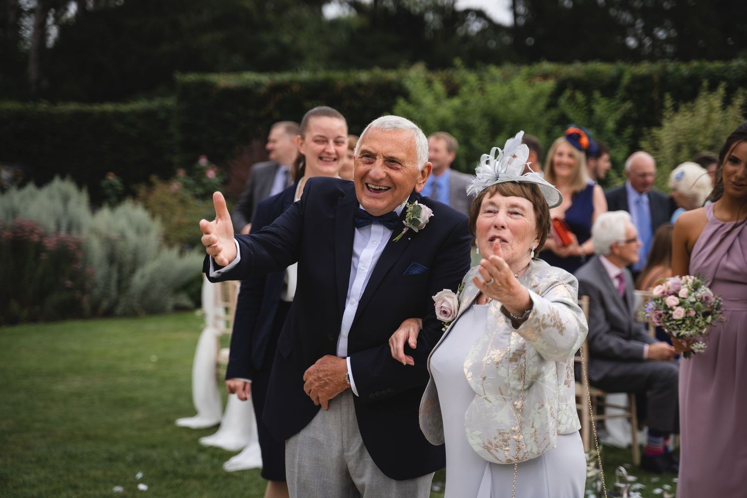 A couple celebrates during their outdoor garden wedding ceremony as guests look on and applaud.