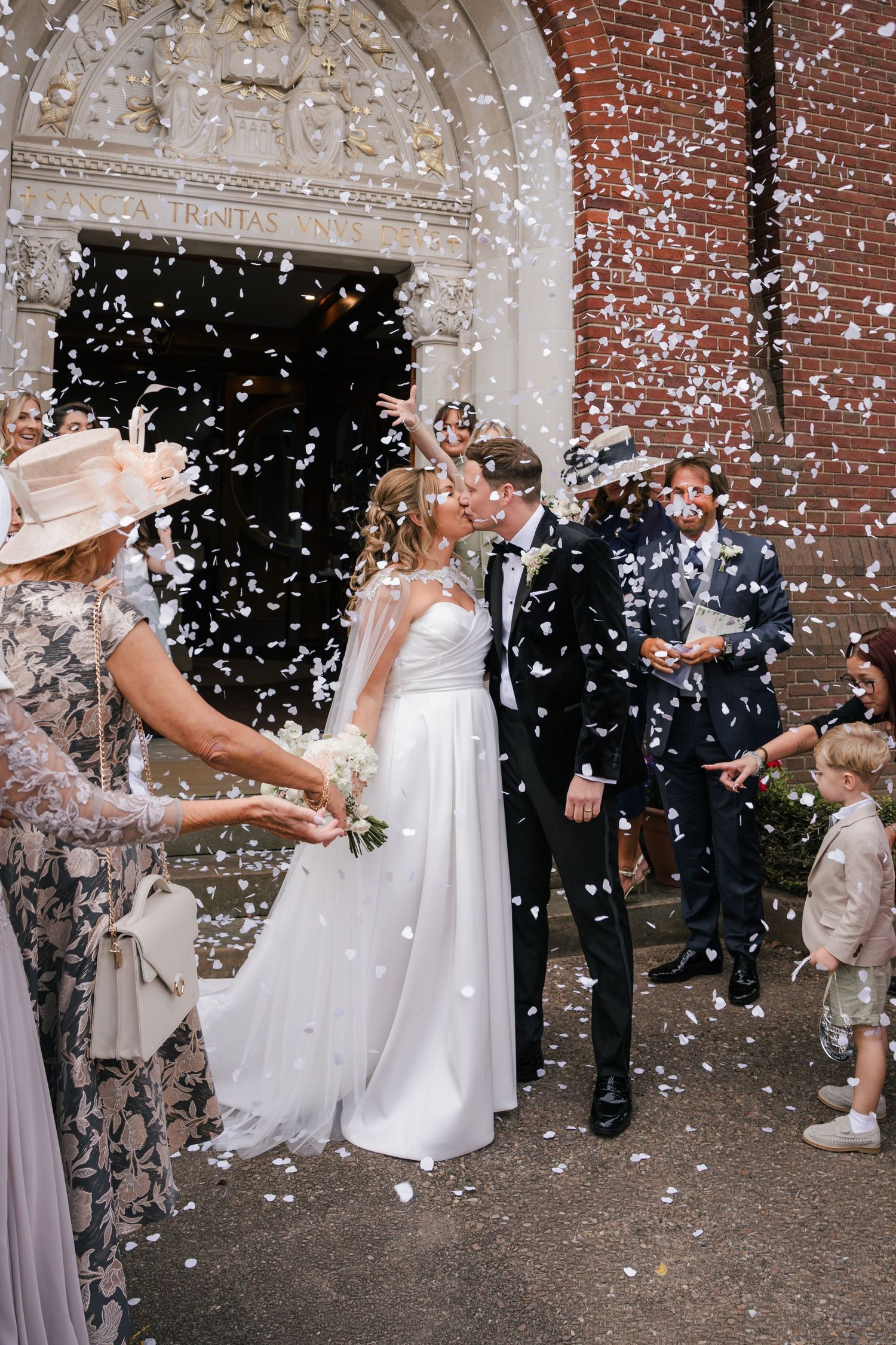Wedding couple celebrates under a shower of white confetti outside a brick church building in a sequence of joyful moments.