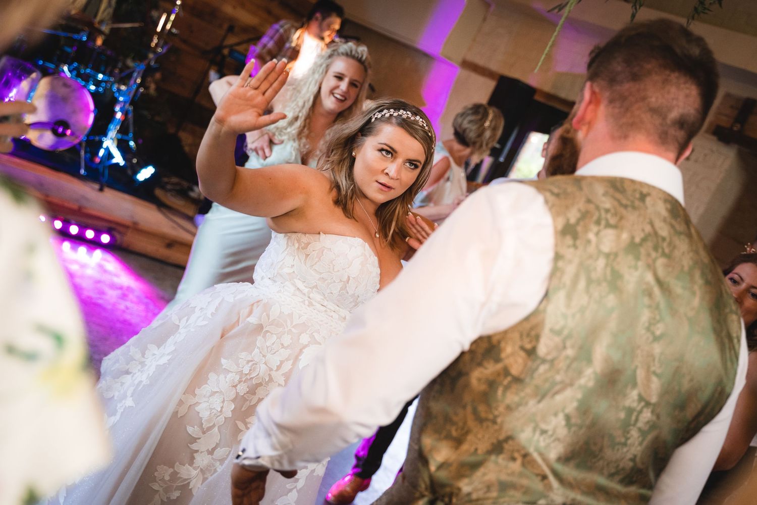 Wedding guests dance and celebrate on a lively dance floor illuminated by purple lighting at an evening reception.