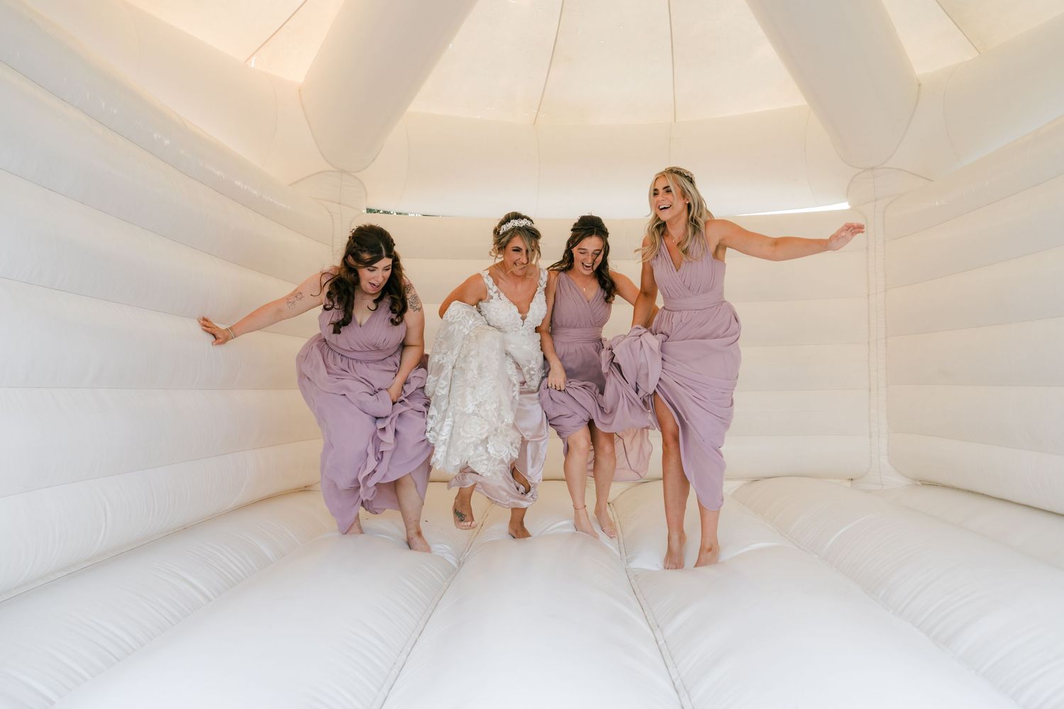 A group in matching purple and white outfits sits together on a white bouncy house floor during a fun party celebration.