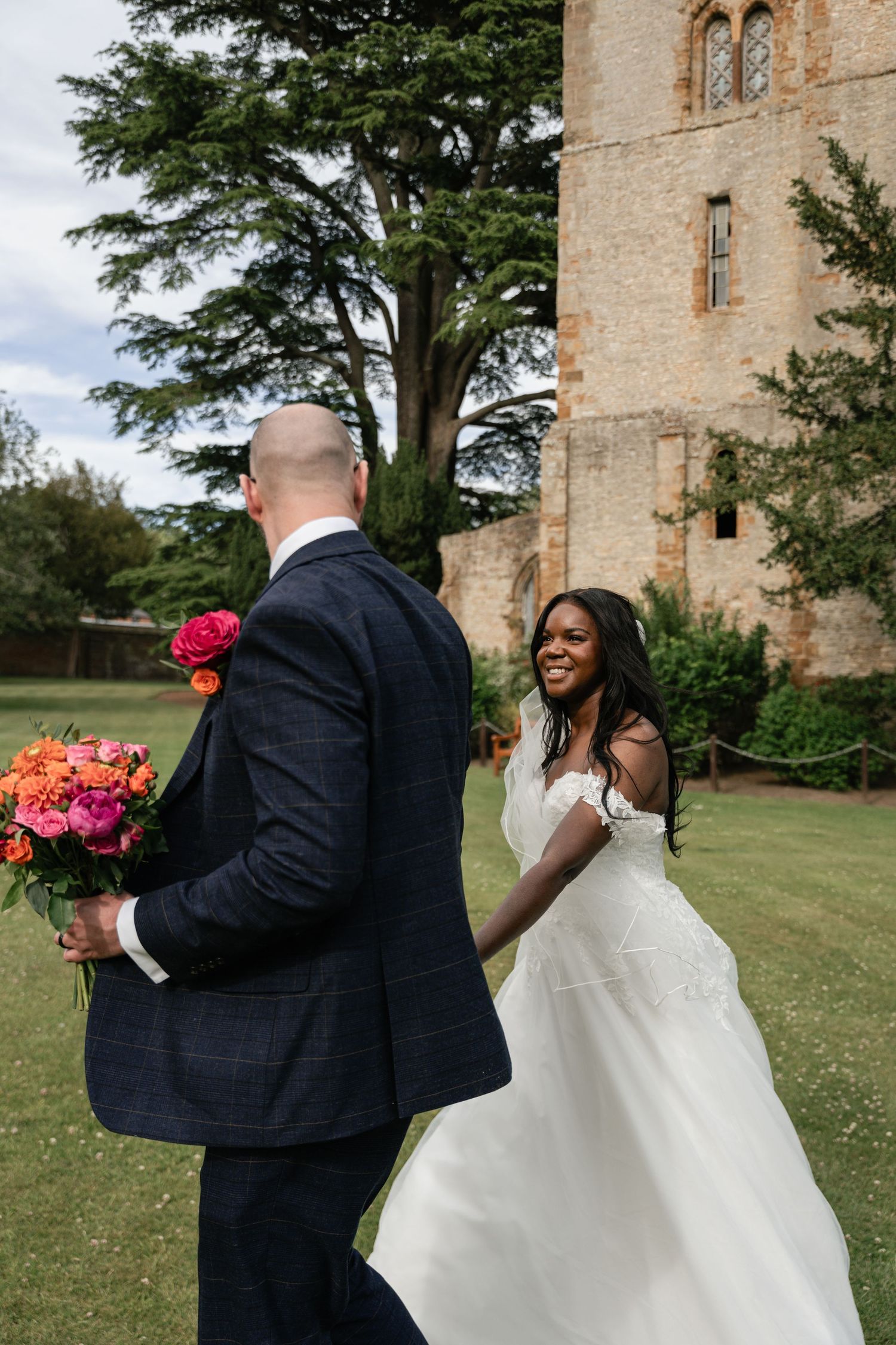 A joyful wedding moment captured outside a historic stone castle with a beautiful bouquet of pink and coral flowers.