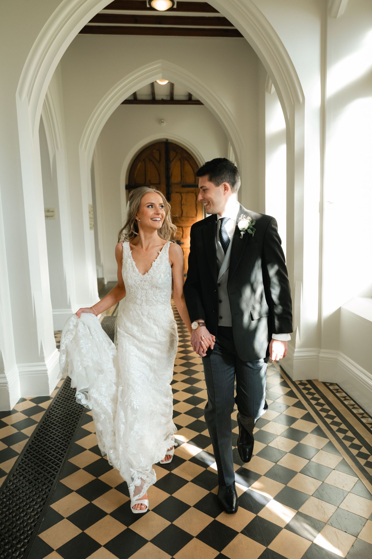A couple walks together through an elegant arched hallway with a black and white checkered floor pattern.