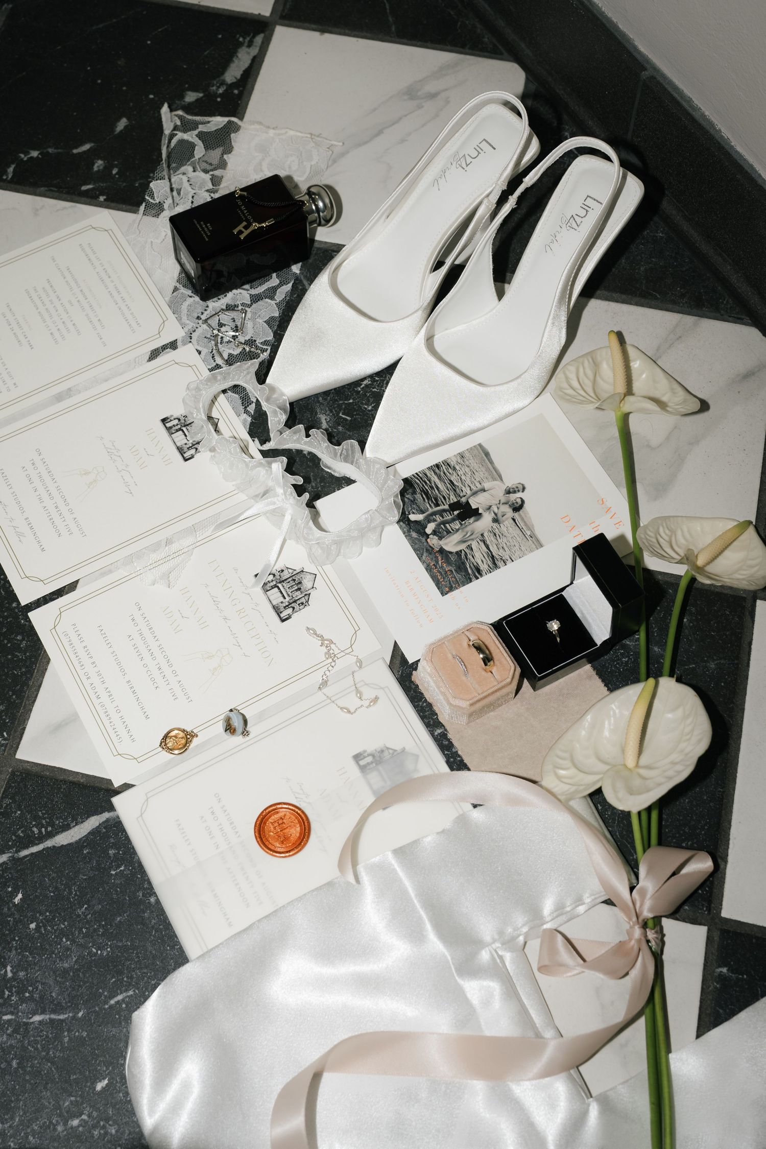 Wedding invitation suite with white flowers and silk ribbon styled on dark marble surface.