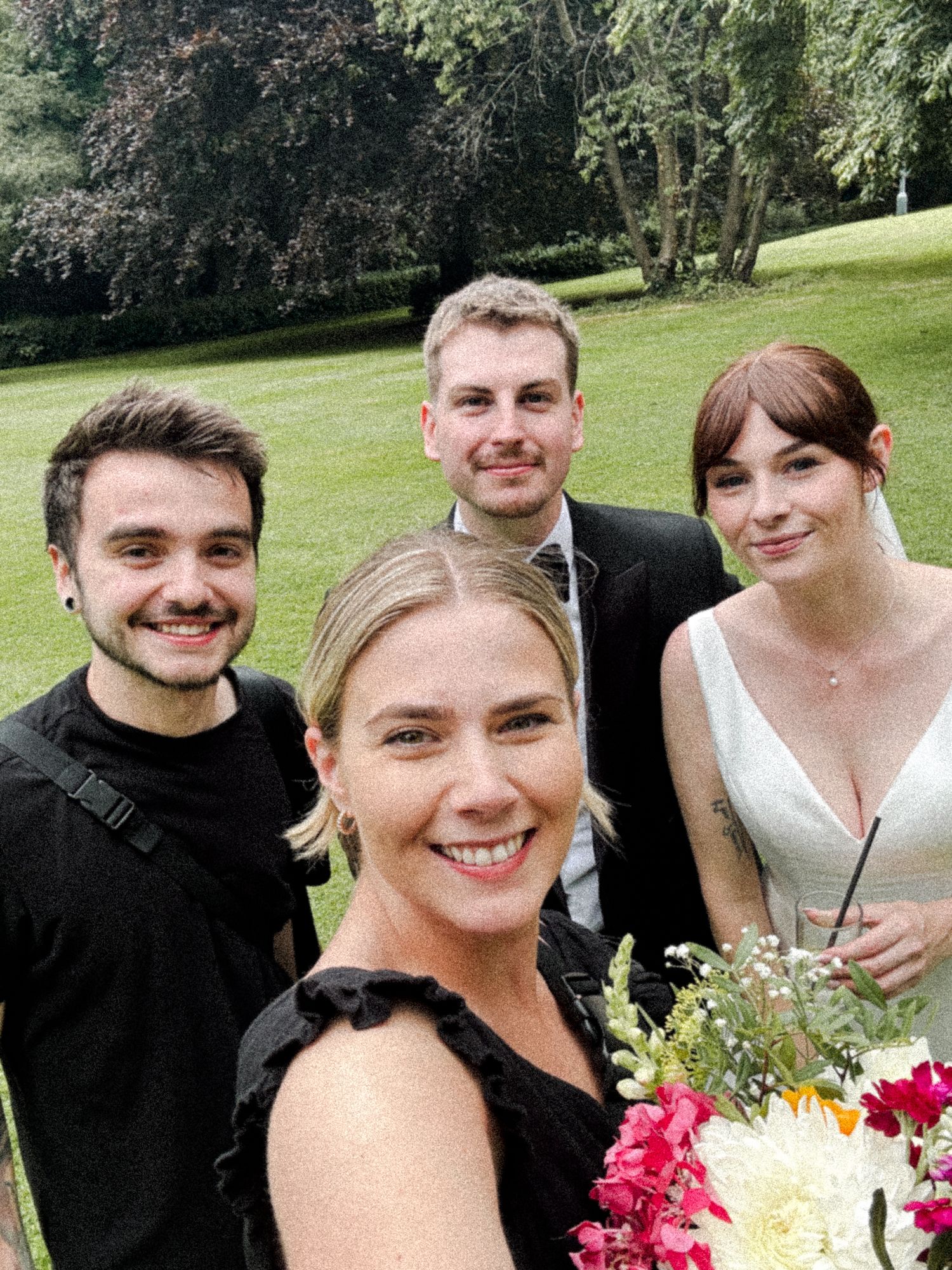 A group of people smiling and posing together outdoors with a colorful bouquet of flowers on a sunny day.