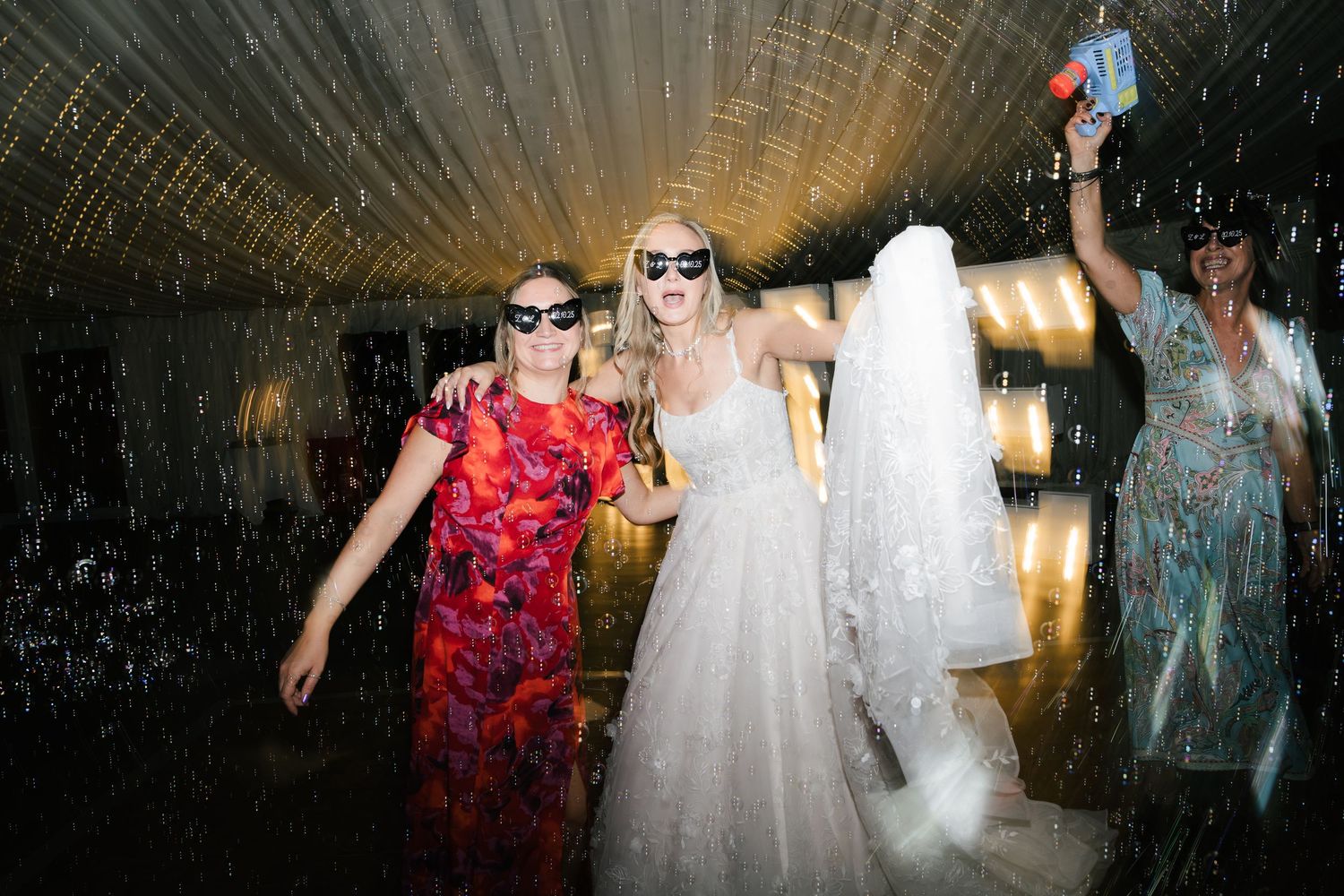 Wedding reception party with guests dancing and celebrating in a dimly lit venue with atmospheric lighting.