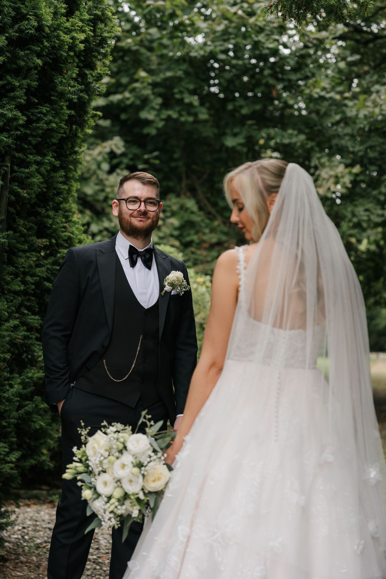 Bride and groom share an intimate first look moment in a lush garden setting with white floral bouquet.