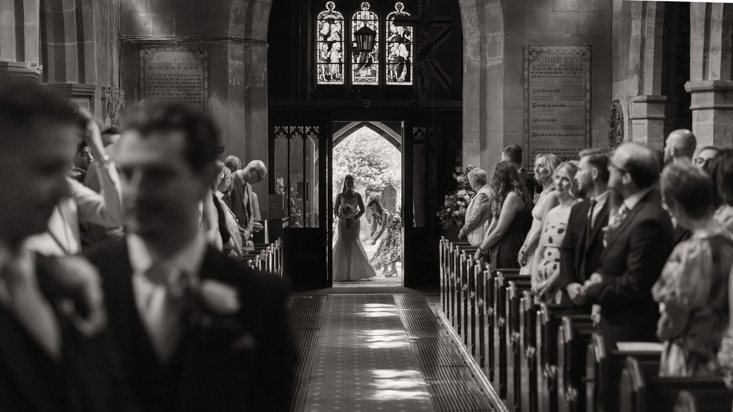 Black and white wedding photo of bride and groom at church altar aisle with guests seated in pews.