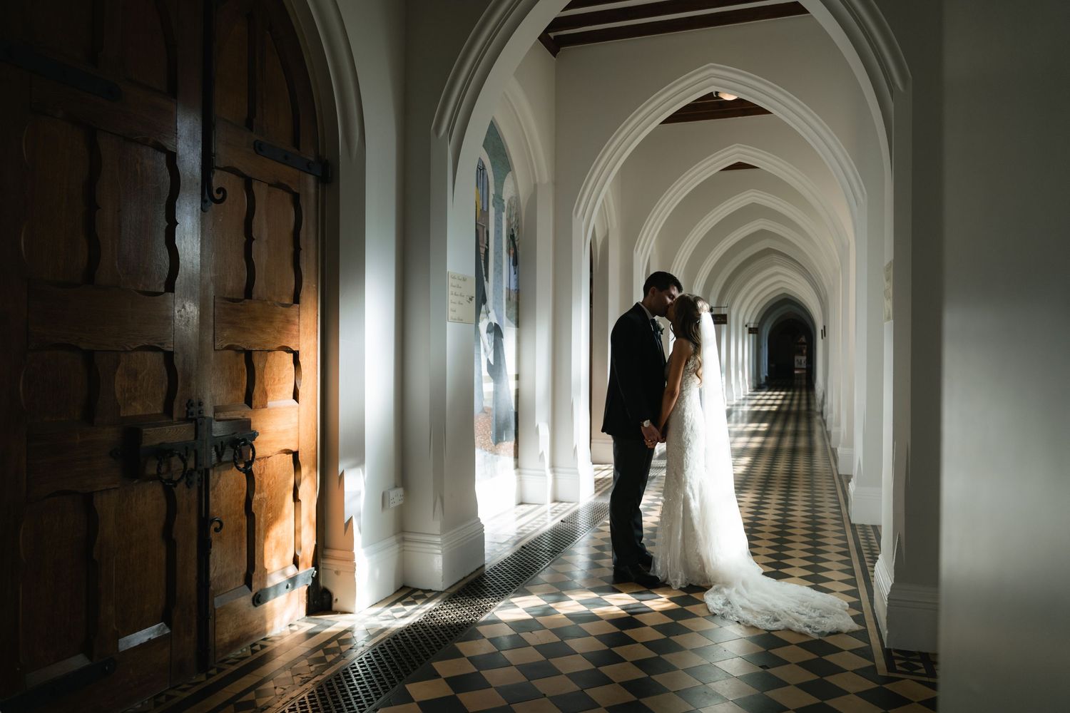 Sunlight streams through arched windows in a historic church corridor with black and white checkered floors.