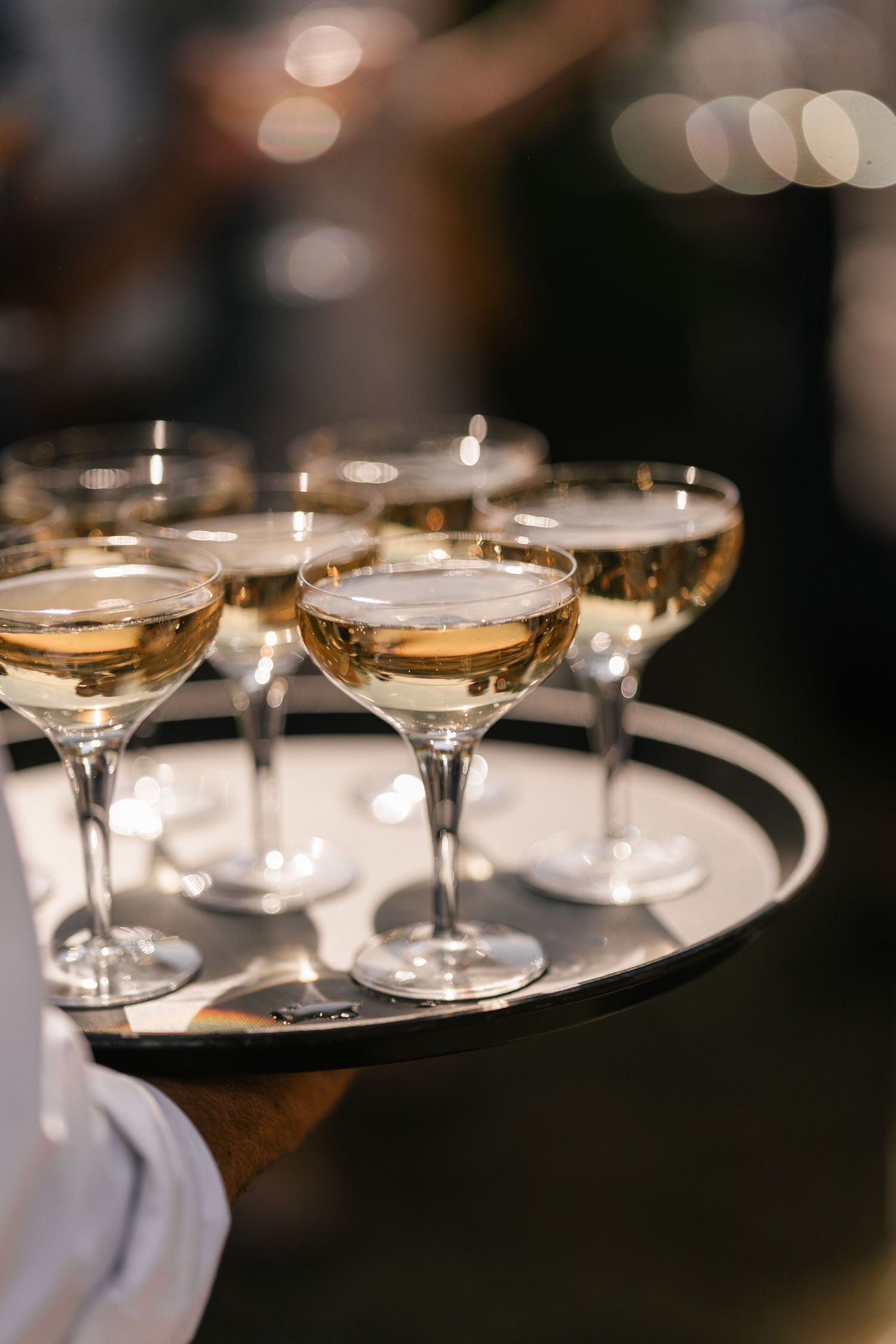 Elegant champagne coupe glasses arranged on silver serving tray in dim lighting.