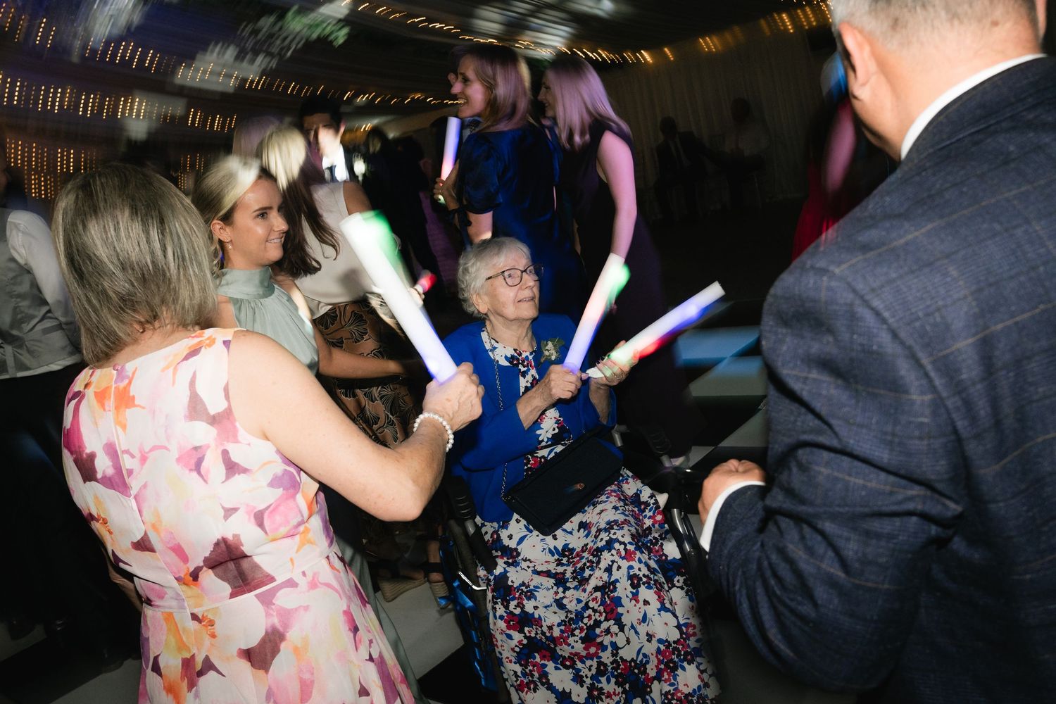 People dancing and enjoying themselves at a wedding reception with colorful lights and decorations.
