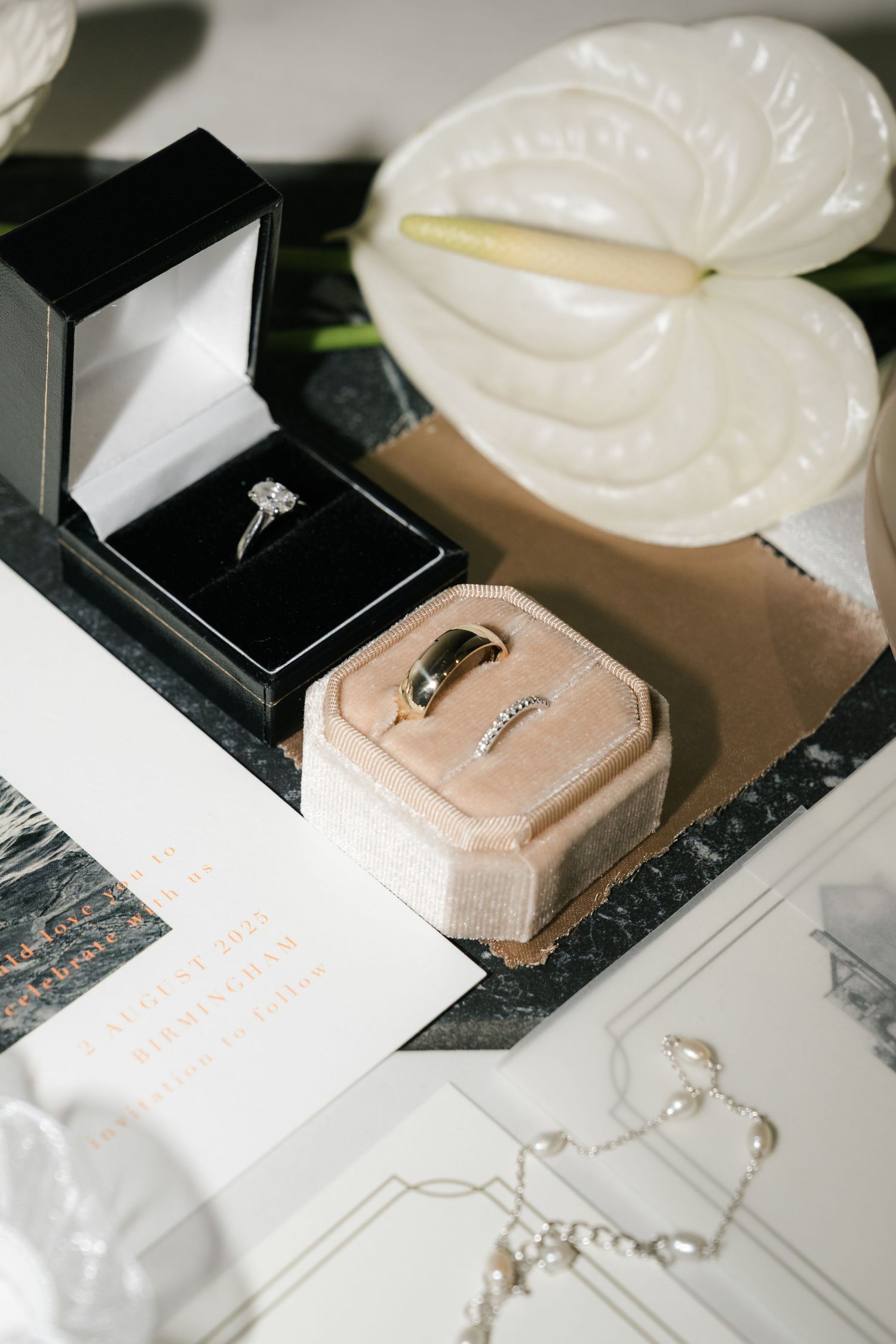 Wedding rings and jewelry displayed in black velvet boxes on a white surface with elegant styling.