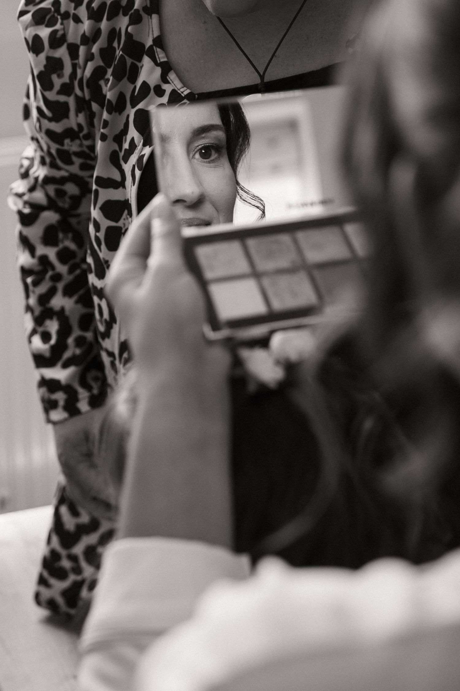 Close-up black and white photo of someone applying mascara to their eyelashes in a bathroom mirror.