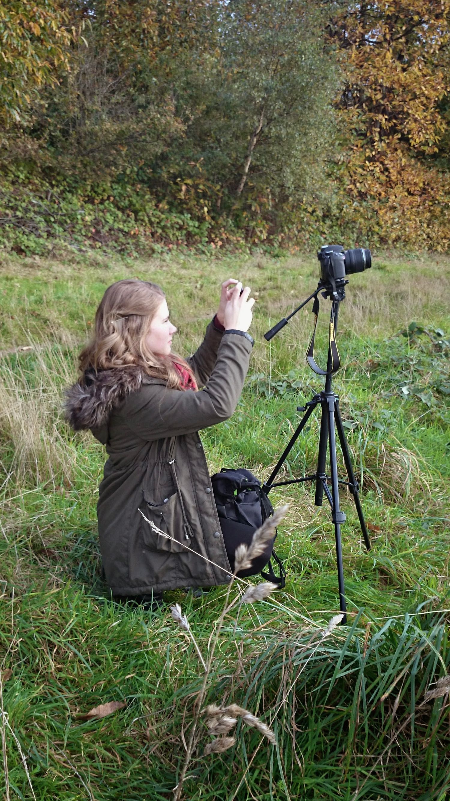 A photographer adjusts camera settings on a tripod in autumn grassland.