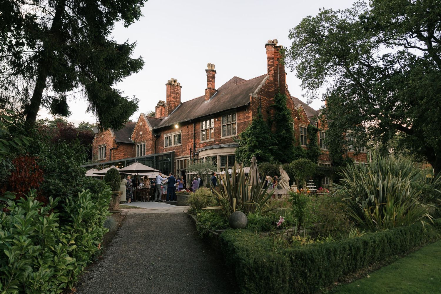 A charming English village street lined with traditional brick houses and lush gardens on a cloudy day.