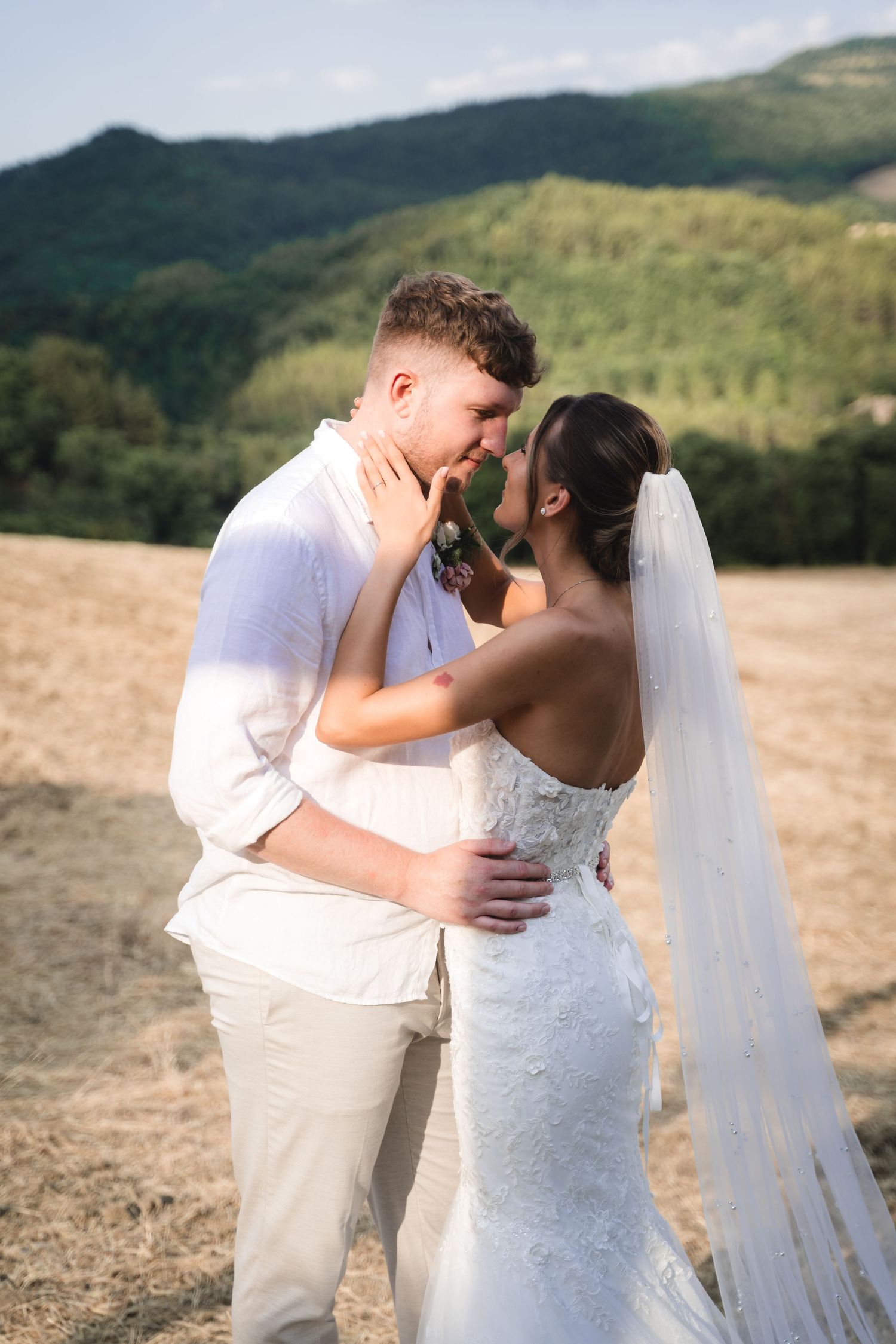 A romantic wedding couple shares intimate kisses against a backdrop of rolling mountain hills during golden hour.