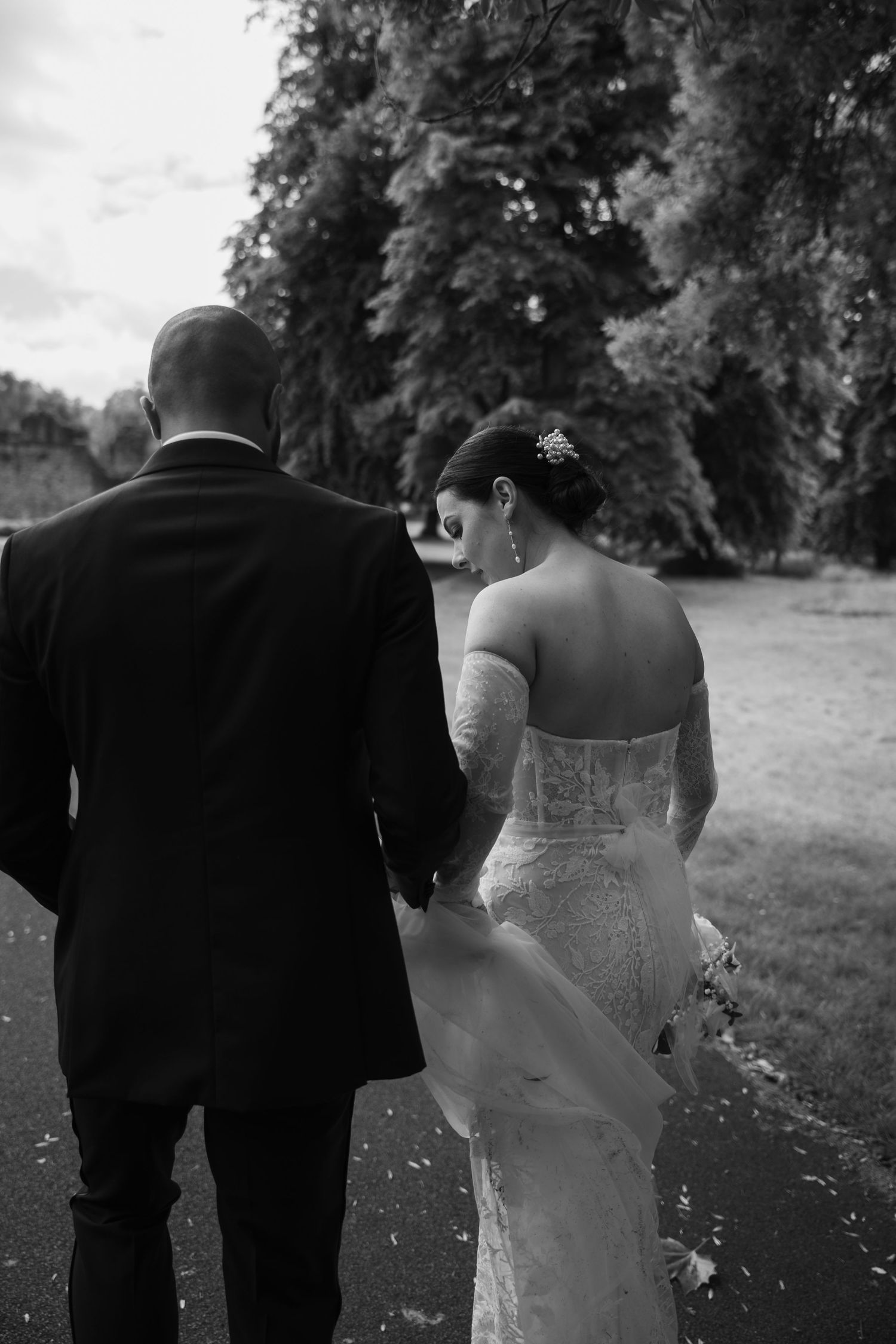 Intimate black and white portrait of newlyweds walking together showing bride's detailed lace back dress.