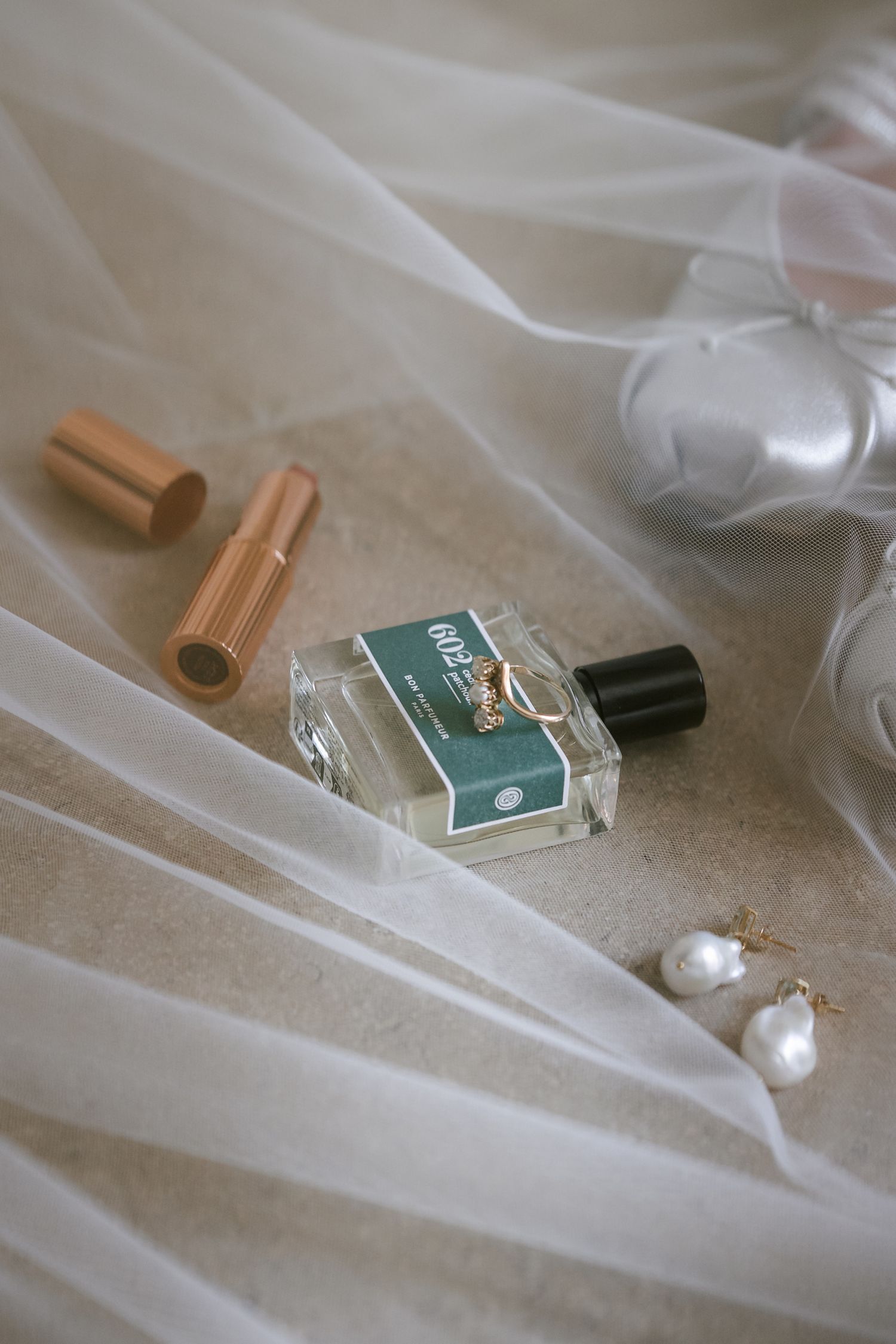 A small perfume bottle and pearl earring rest elegantly on soft white tulle fabric.