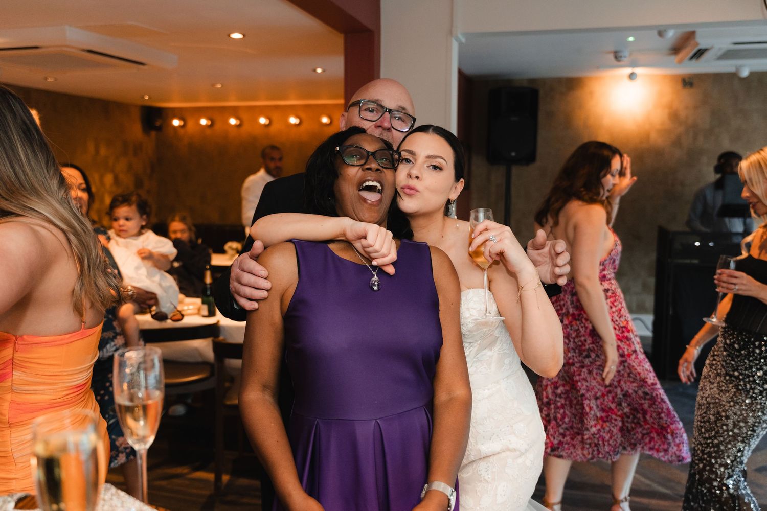 People dance and celebrate at a wedding reception with purple bridesmaid dresses and warm lighting.