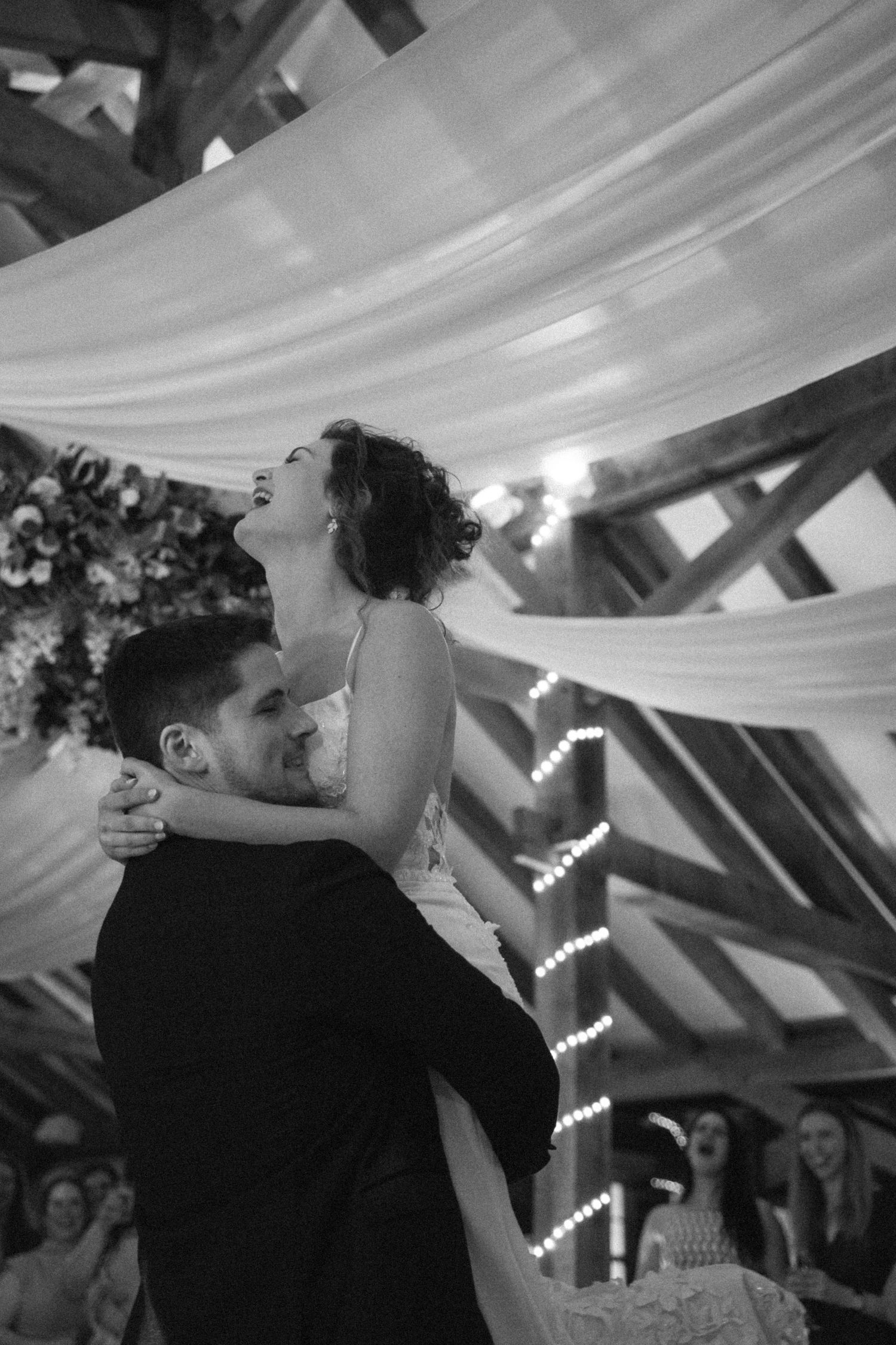 Black and white sequence of a couple's first dance under draped fabric and string lights at a wedding reception.