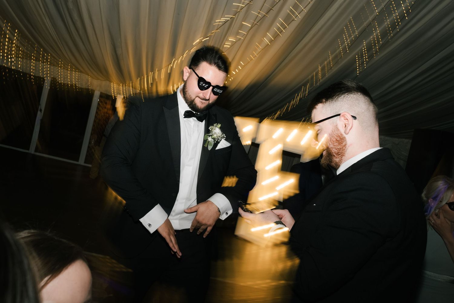 Wedding guests dance and celebrate on a dark dance floor illuminated by dramatic lighting effects.