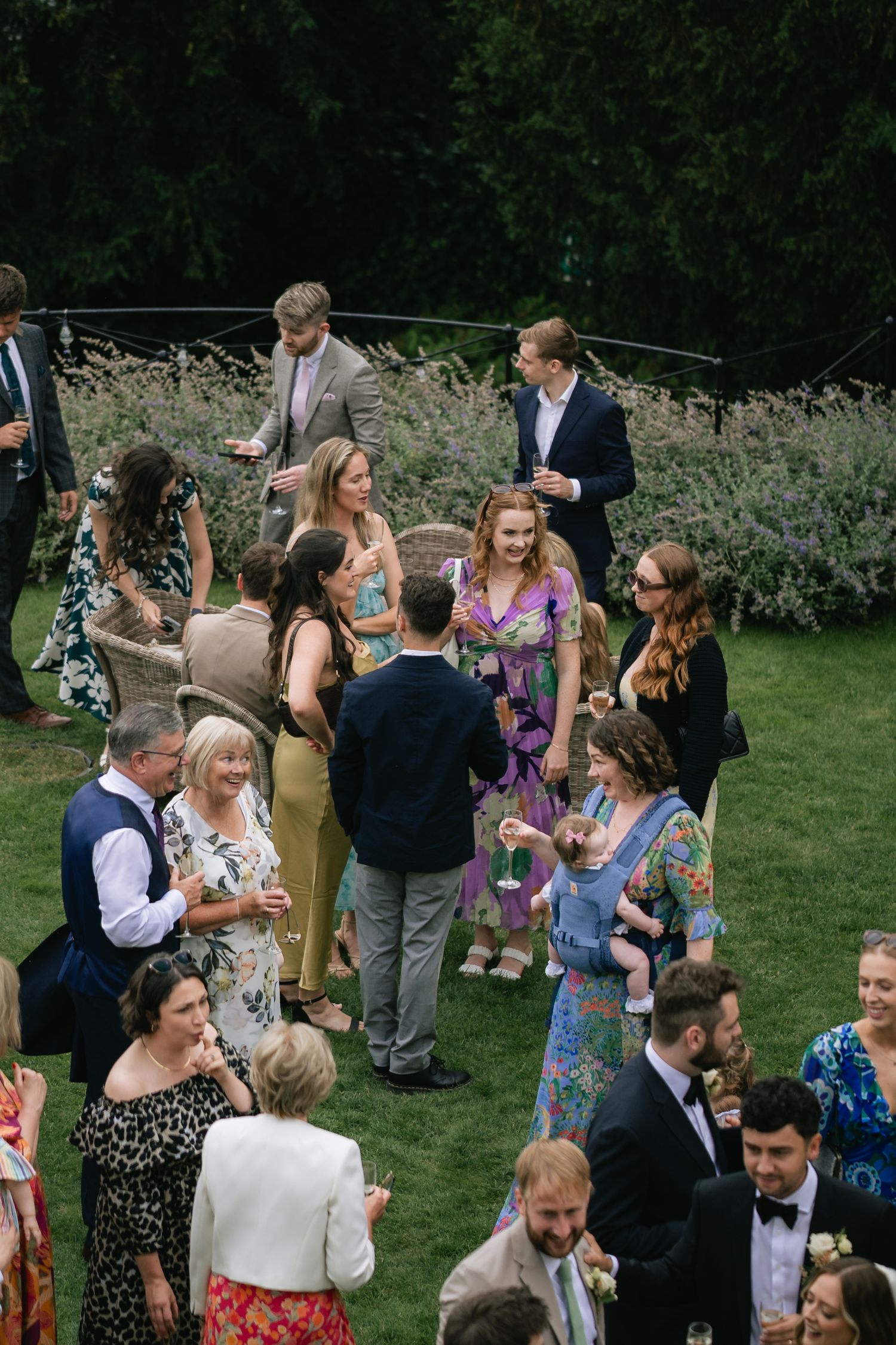 Wedding guests gather on a lush green lawn during an outdoor reception celebration.