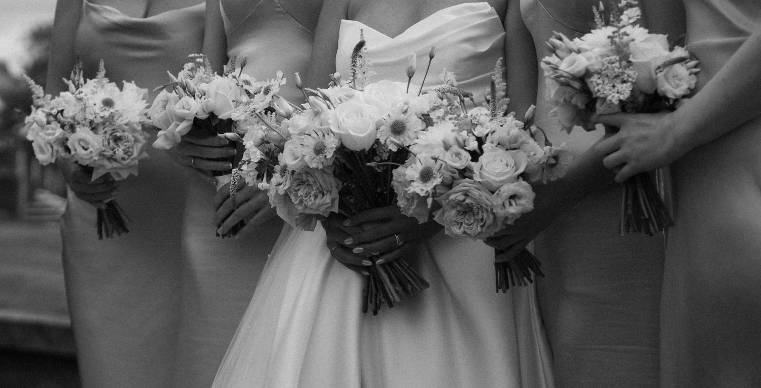 Black and white photo of wedding bouquets held by bridesmaids wearing matching dresses.