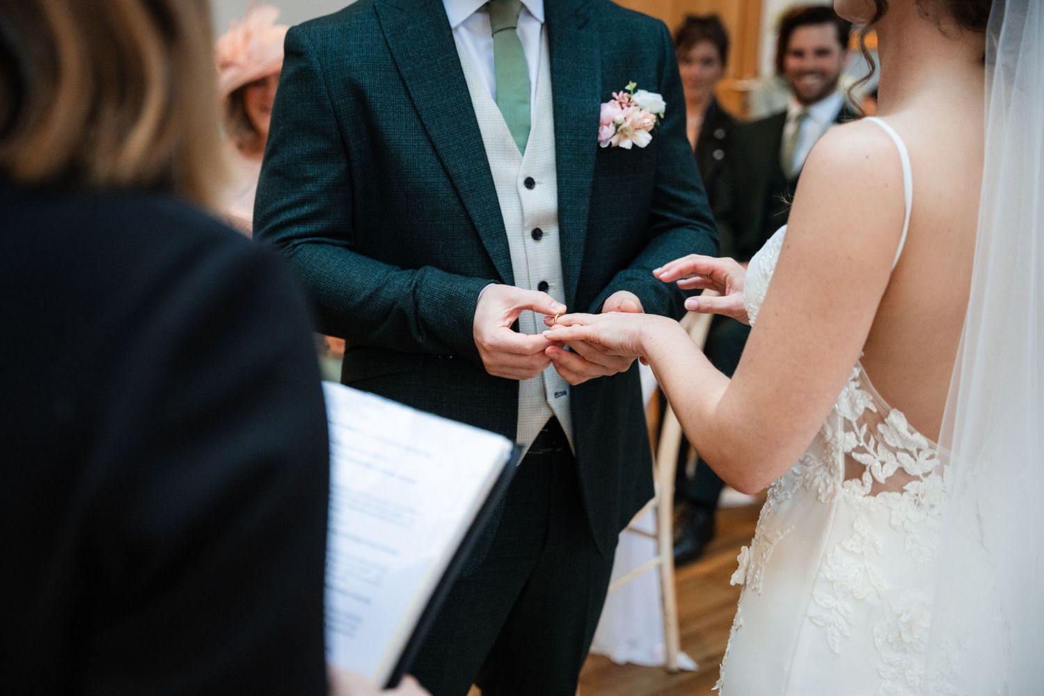 Couple exchanging rings during an elegant indoor wedding ceremony surrounded by guests.