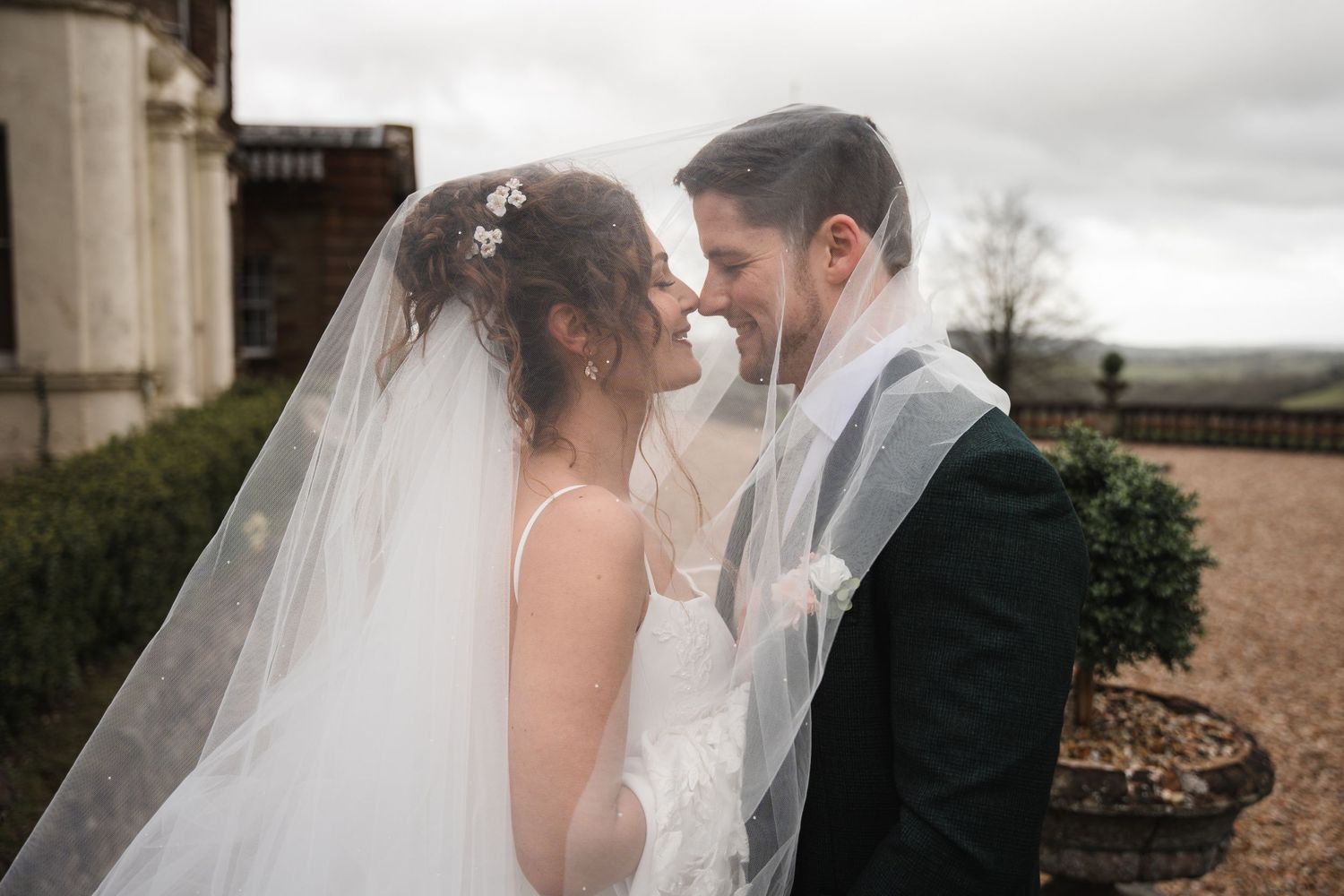 A romantic wedding couple shares an intimate moment under a flowing veil during their outdoor ceremony.