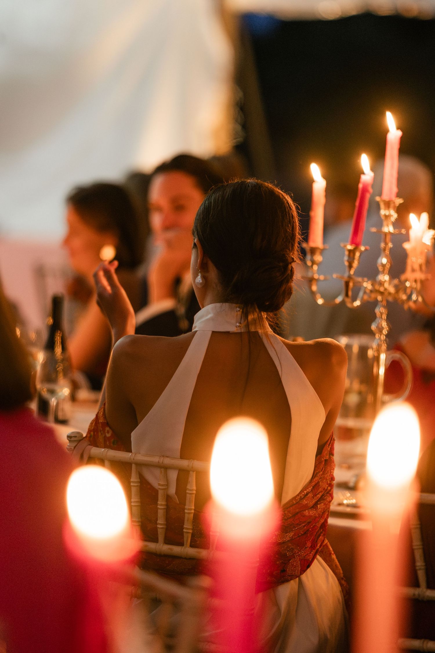 Candlelit dinner scene with elegant candelabras and guests seated at a formal table in warm ambient lighting.