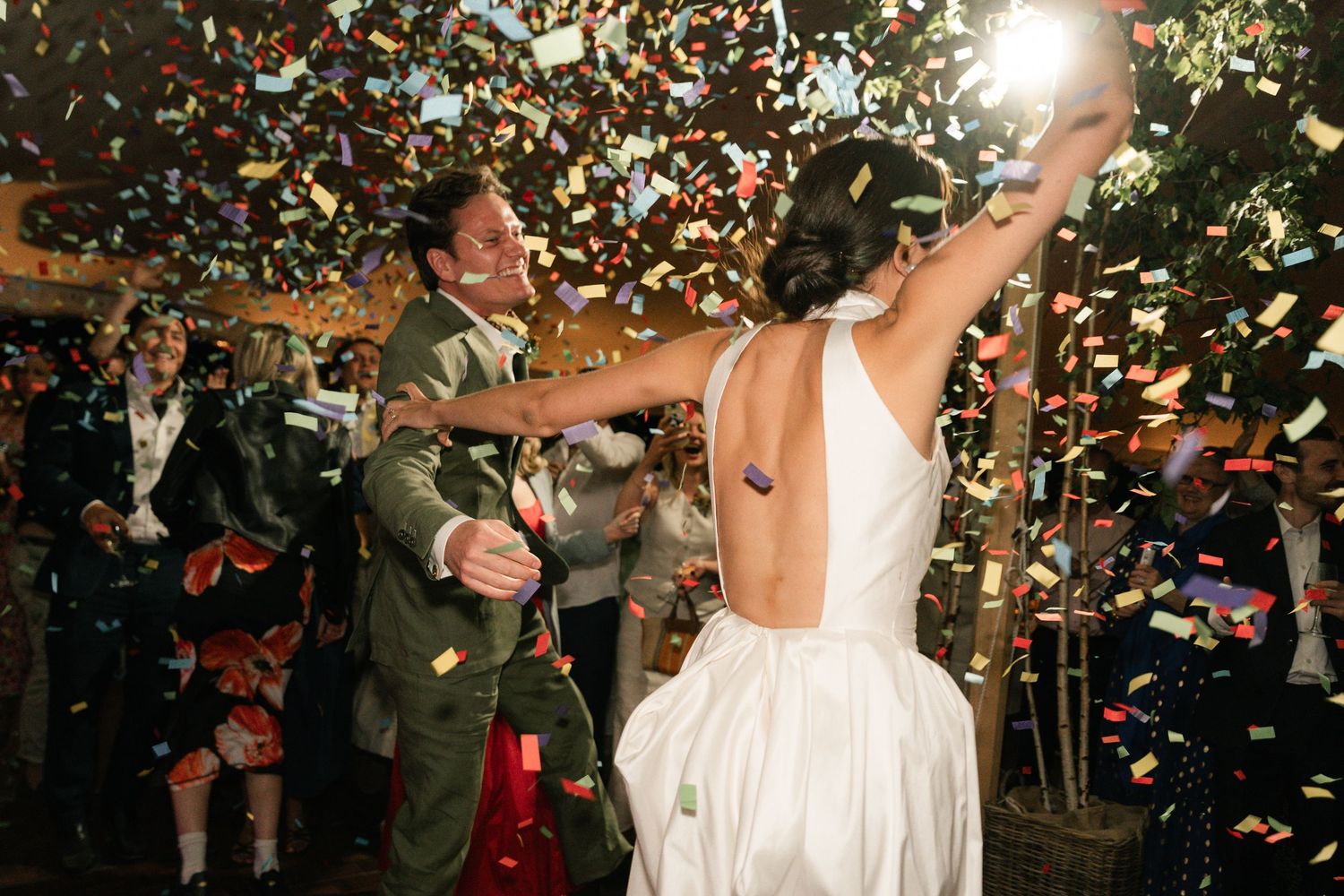 Couple celebrates on dance floor with confetti falling during wedding reception party in evening lighting.