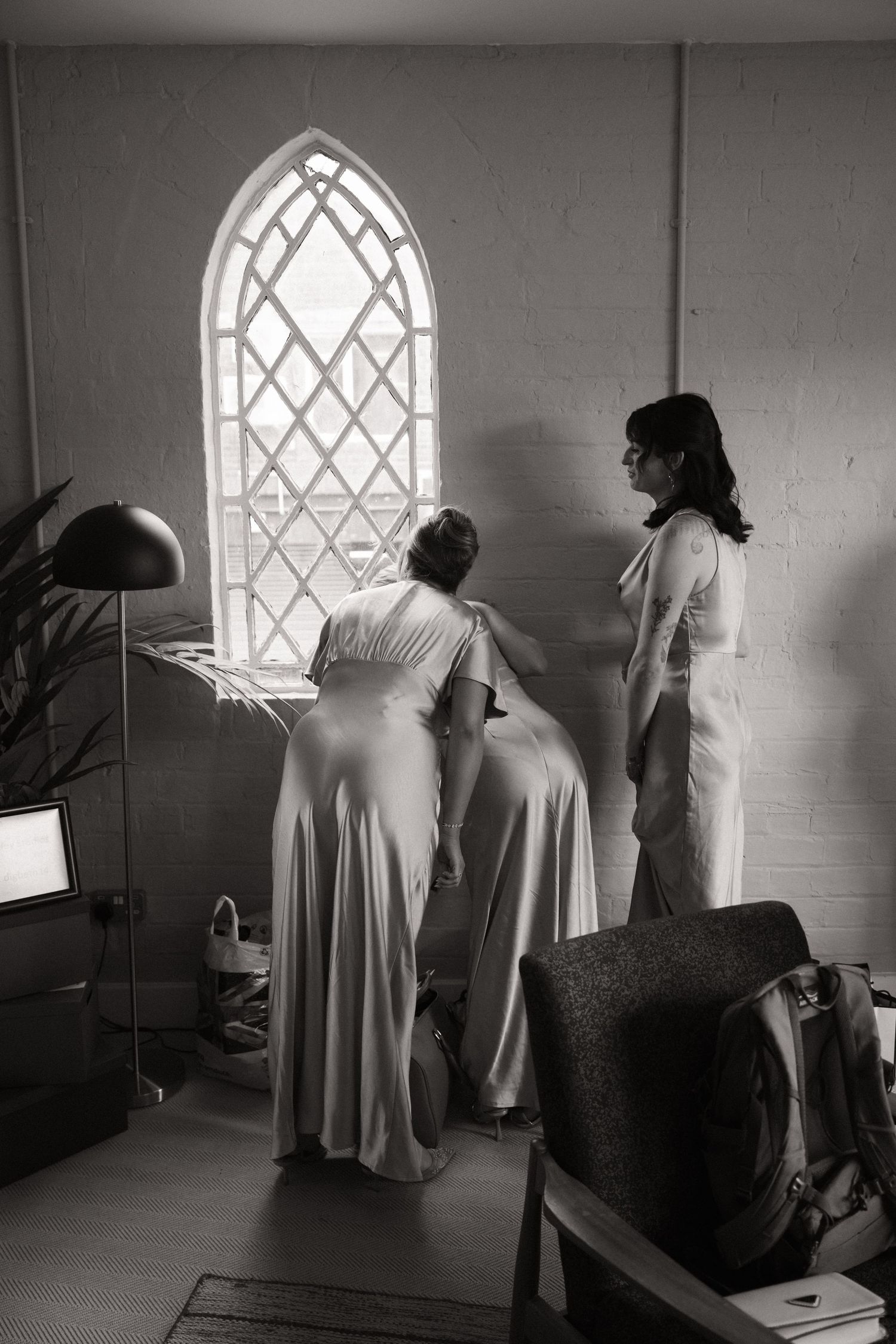 Black and white image of people in light colored dresses looking through a diamond-paned church window.