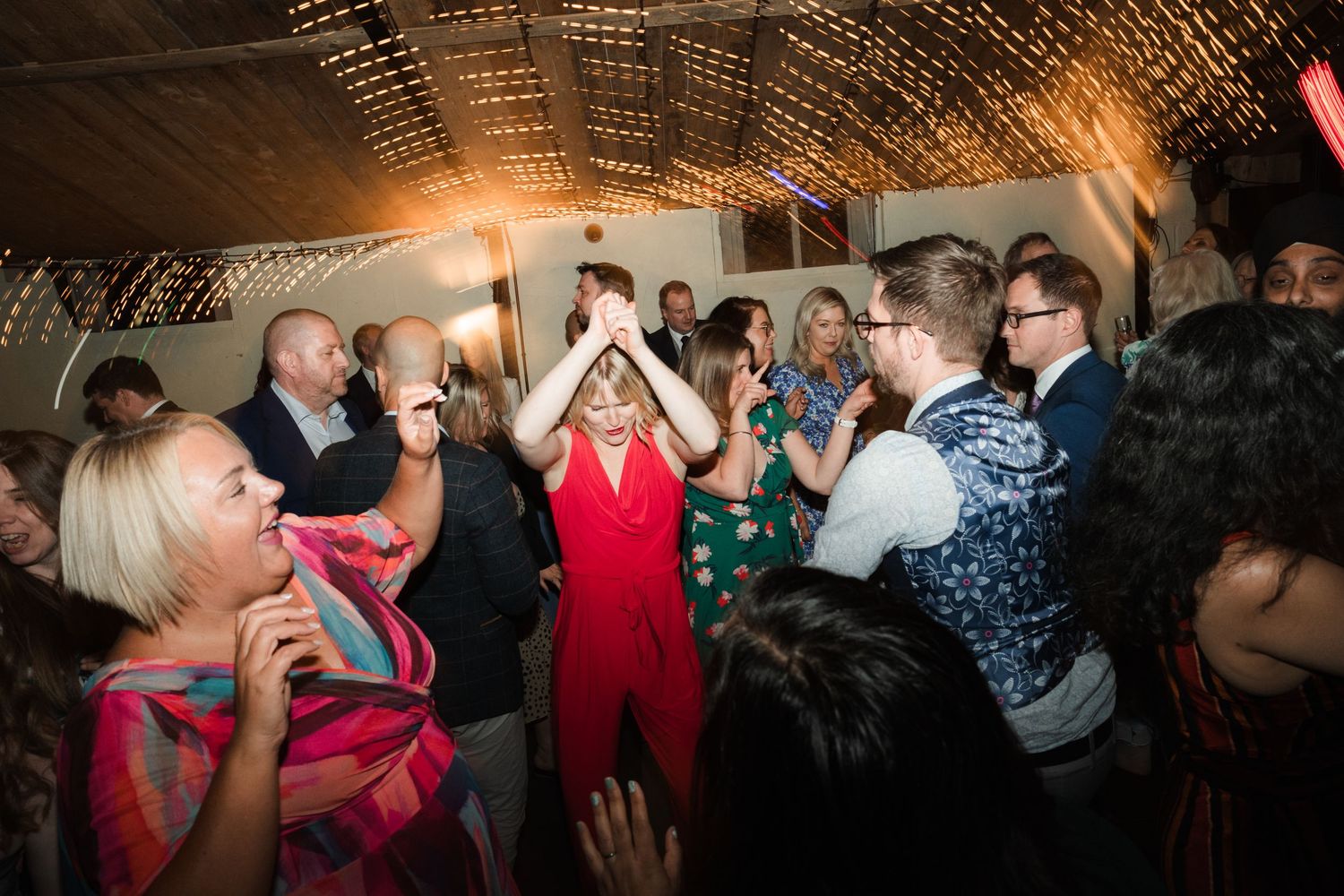 Dance party scene at wedding reception with string lights overhead.