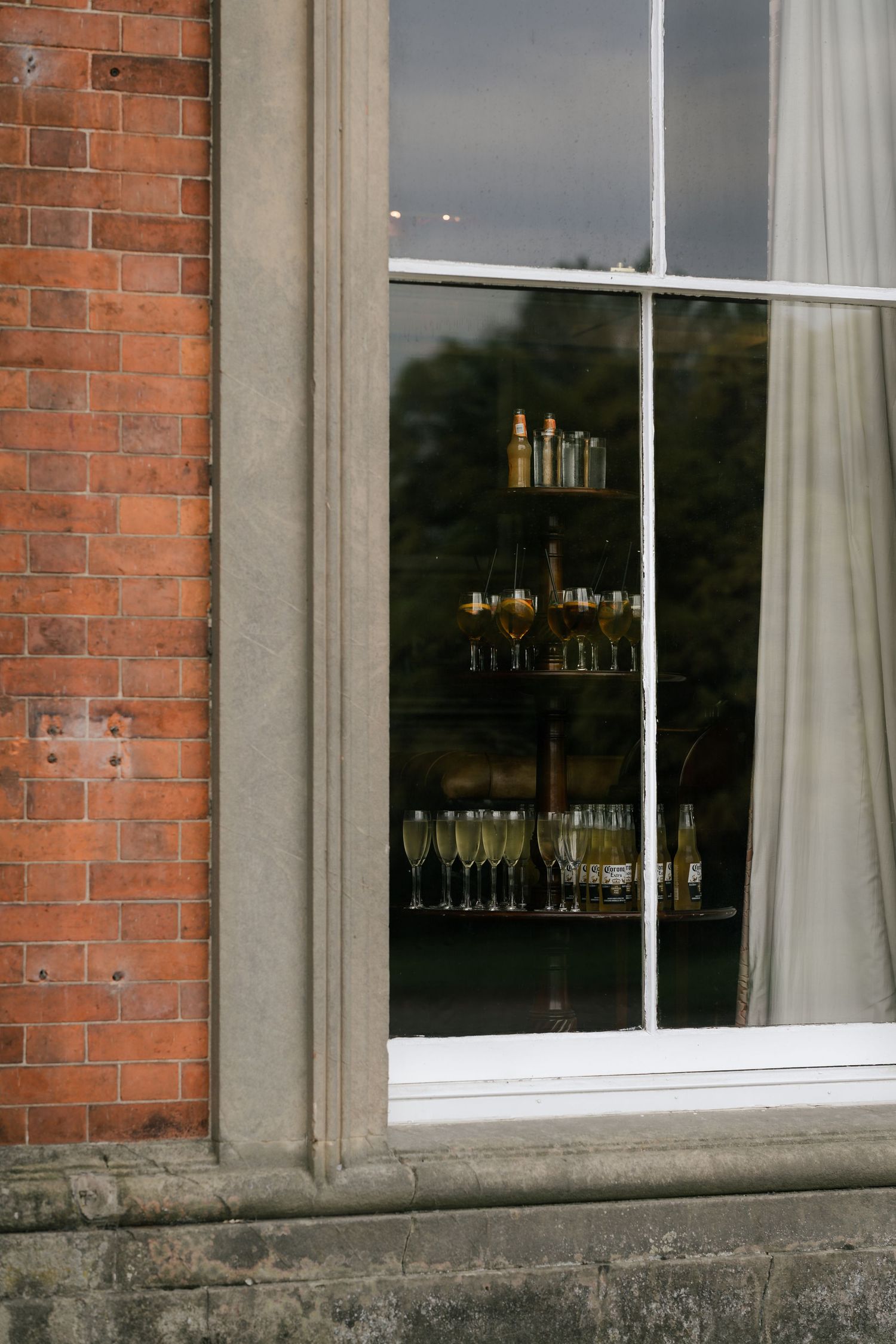 Champagne glasses and bottles visible through a window framed by red brick and stone exterior.