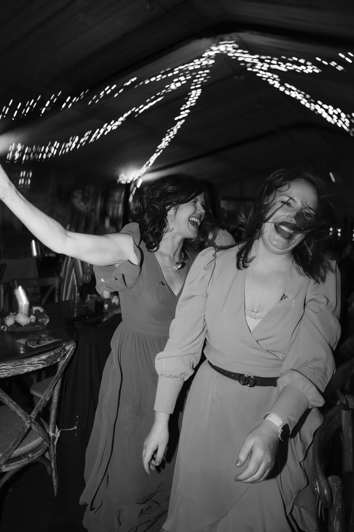Two women dancing joyfully at a party under twinkling lights in black and white photography.