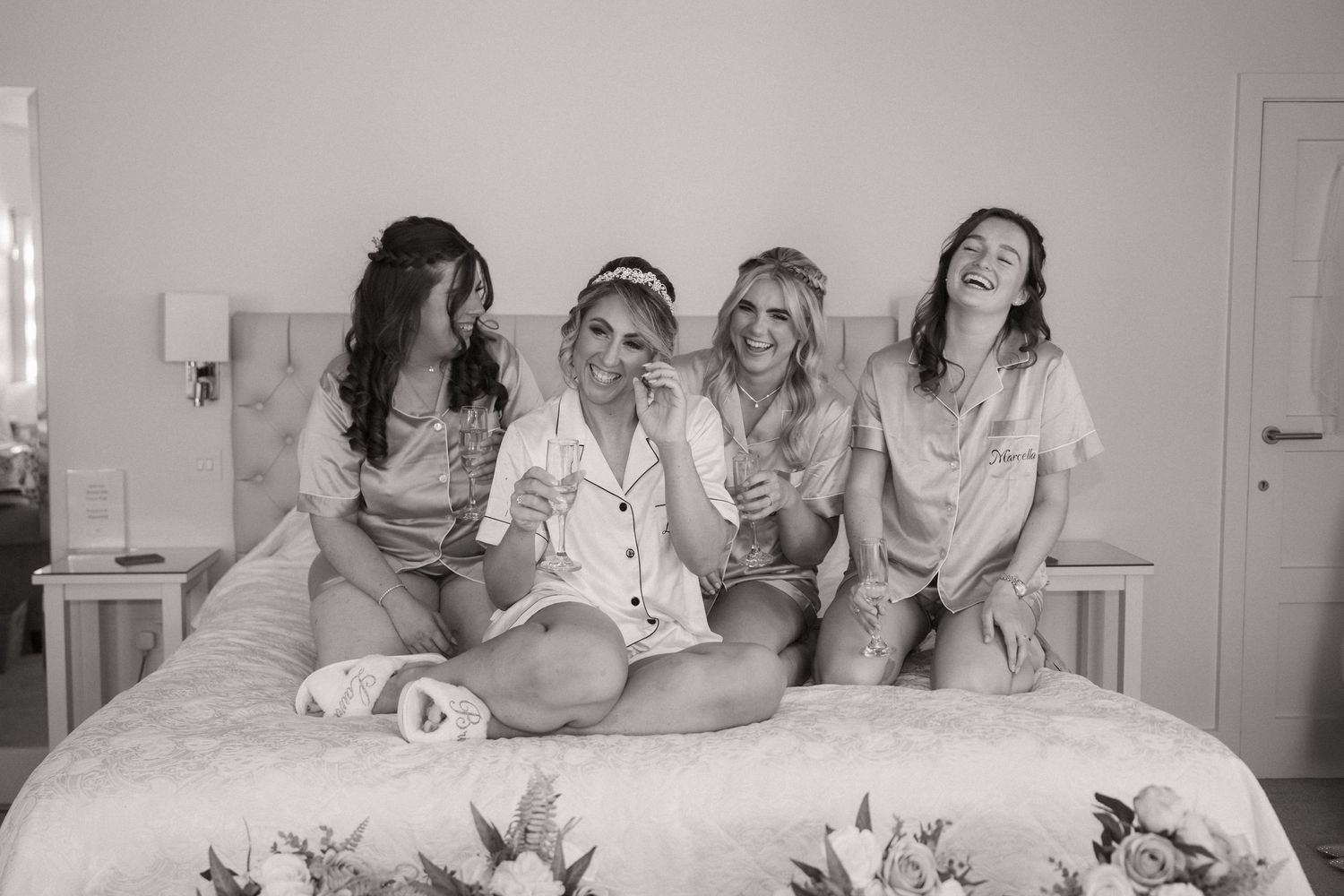 A black and white photo of friends laughing together while sitting on a floral bedspread.