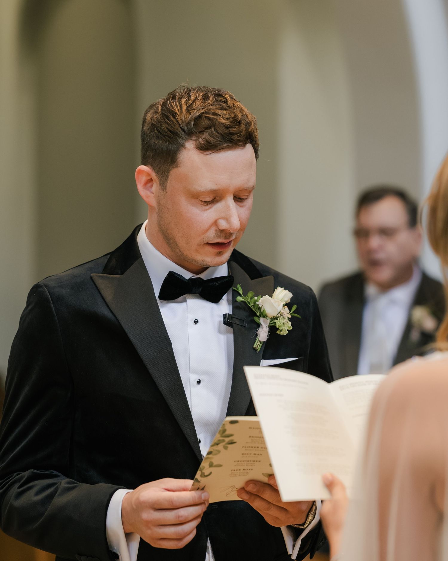 Groom in black tuxedo reads emotional letter while getting ready for wedding ceremony.