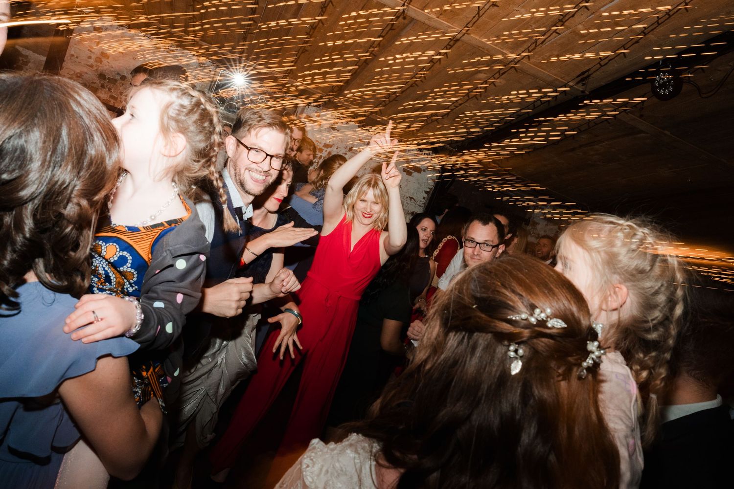 A lively crowd dances and celebrates at a dimly lit party venue with dramatic lighting effects.